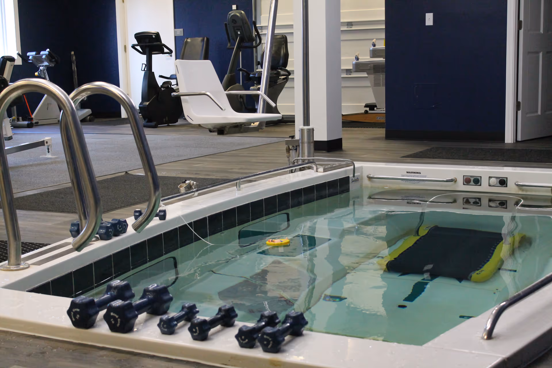 Indoor rehabilitation facility with a therapy pool and exercise equipment in a modern gym area.