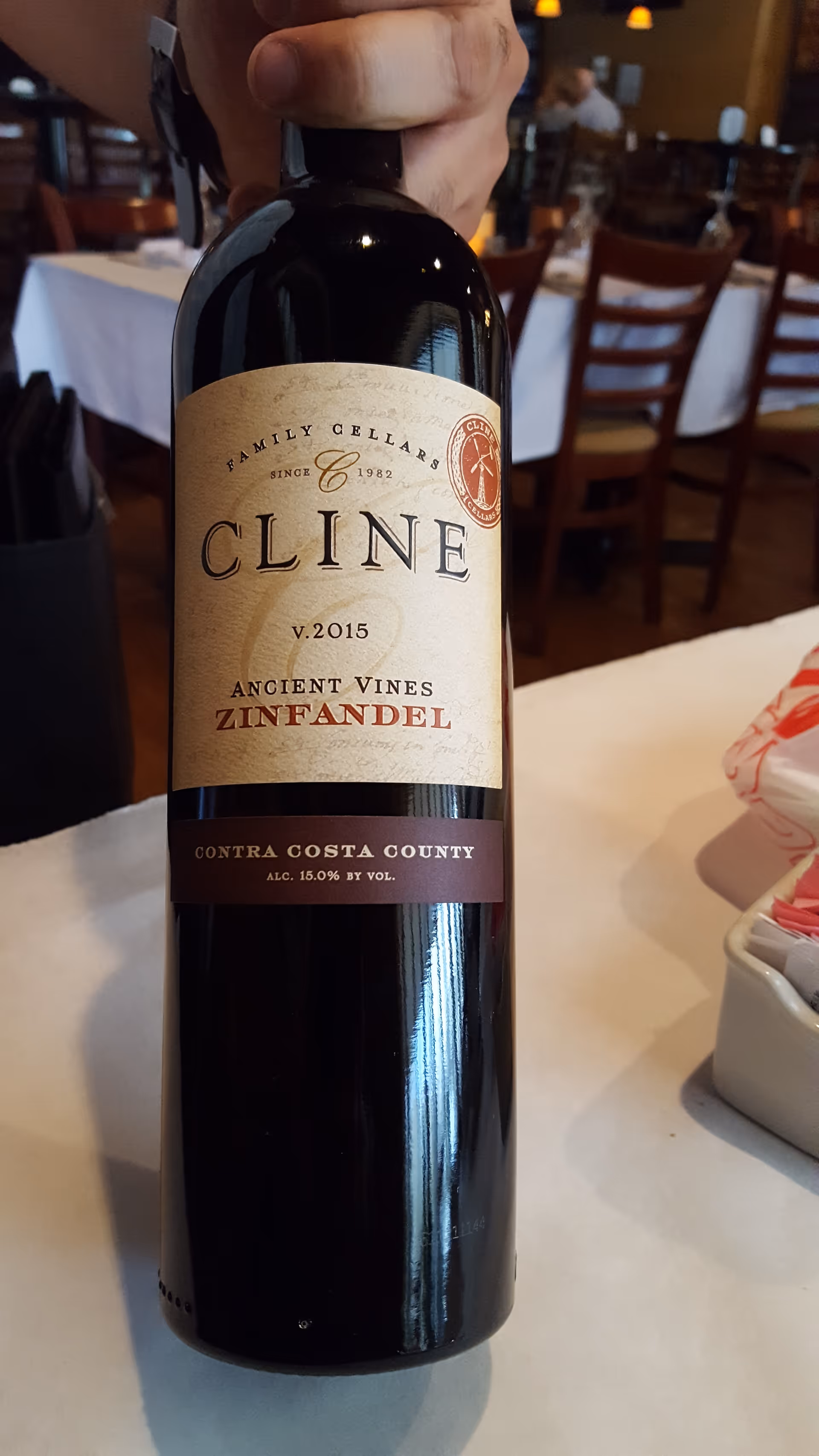 Close-up of a wine bottle held at a restaurant table.