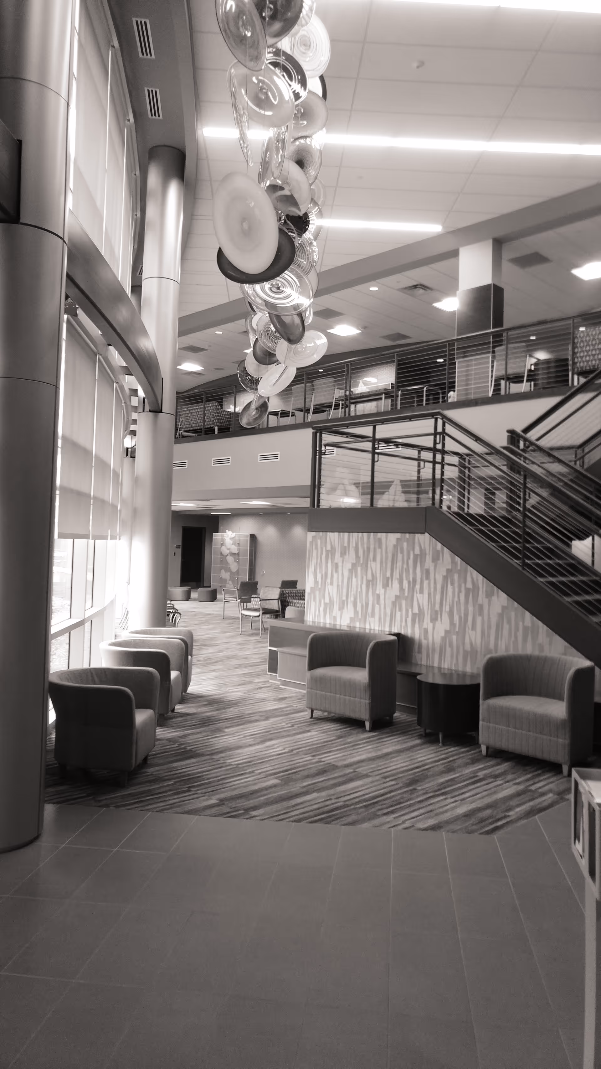 Modern lobby area in grayscale with chairs, a curved staircase, and hanging circular decor.