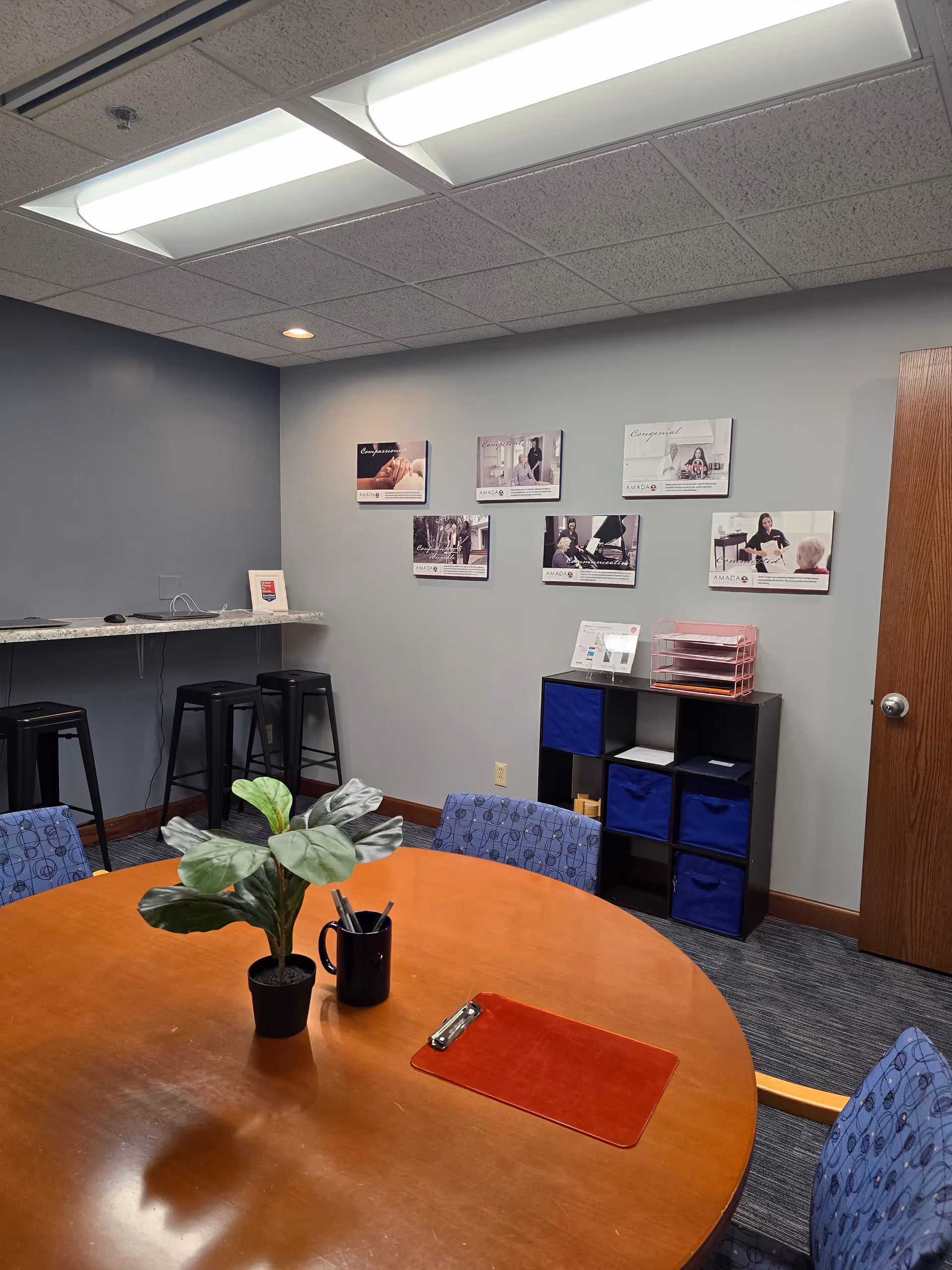 Round wooden table with plant, pens, and brochures in a furnished meeting room.