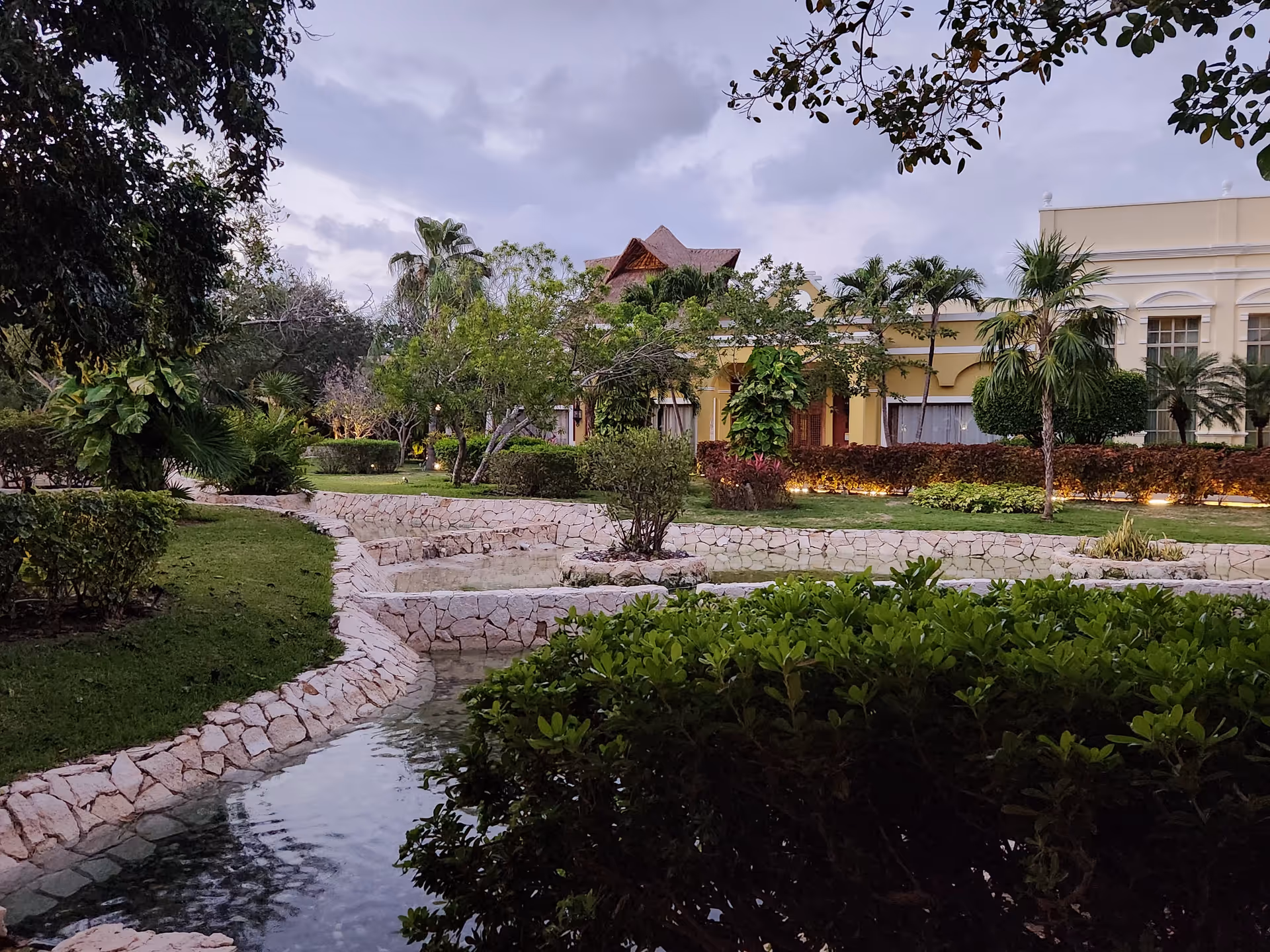 Well-manicured garden with stone paths, a water feature, and a yellow building in the background.