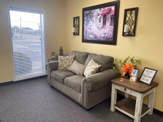 Cozy senior living lounge with gray sofa, cushions, wall art, and a side table.
