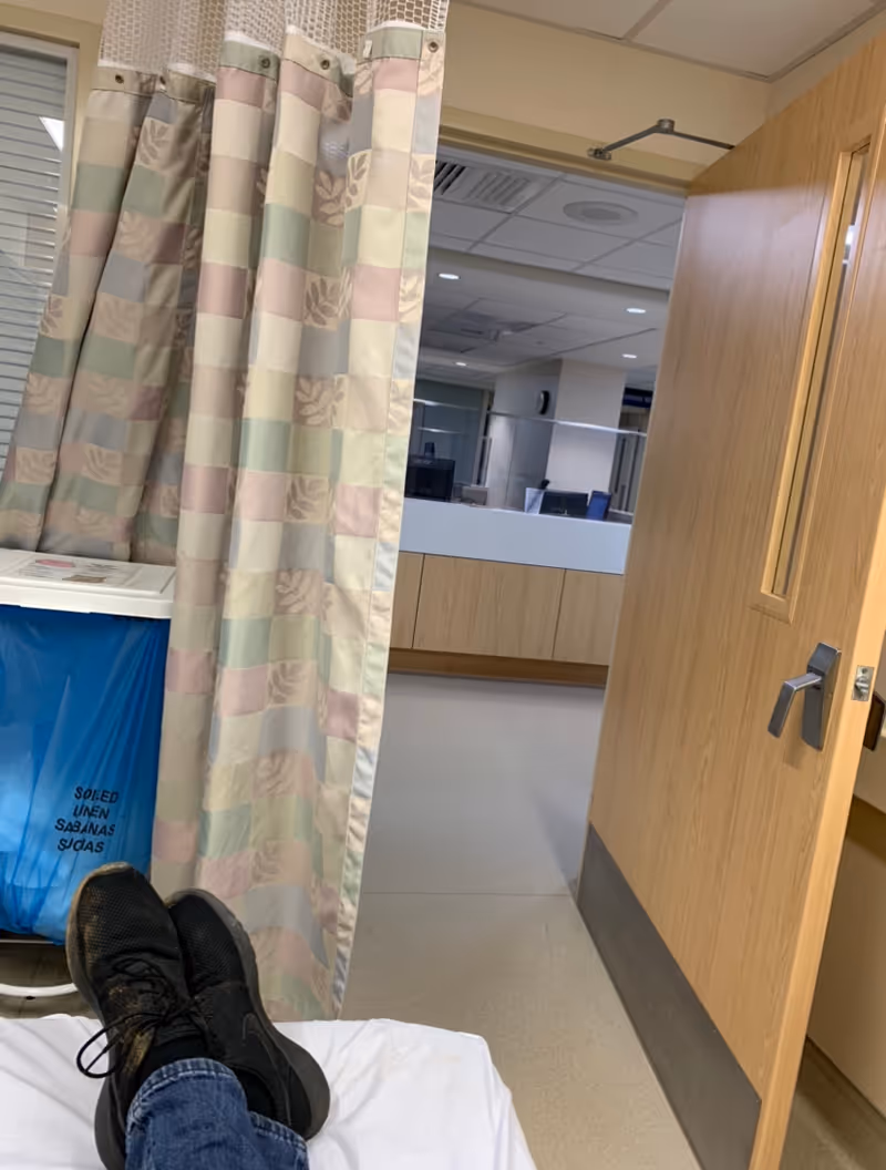 Patient bed area with pastel curtain, feet visible, and open door to hallway.