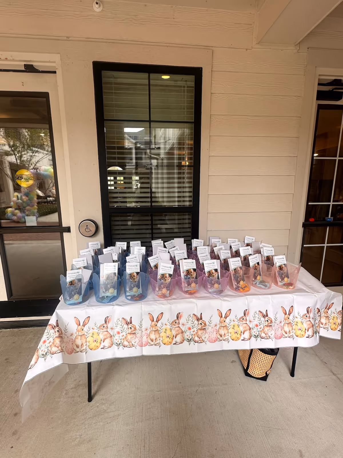 Outdoor table displays pastel Easter gift bags with bunny-themed decorations.