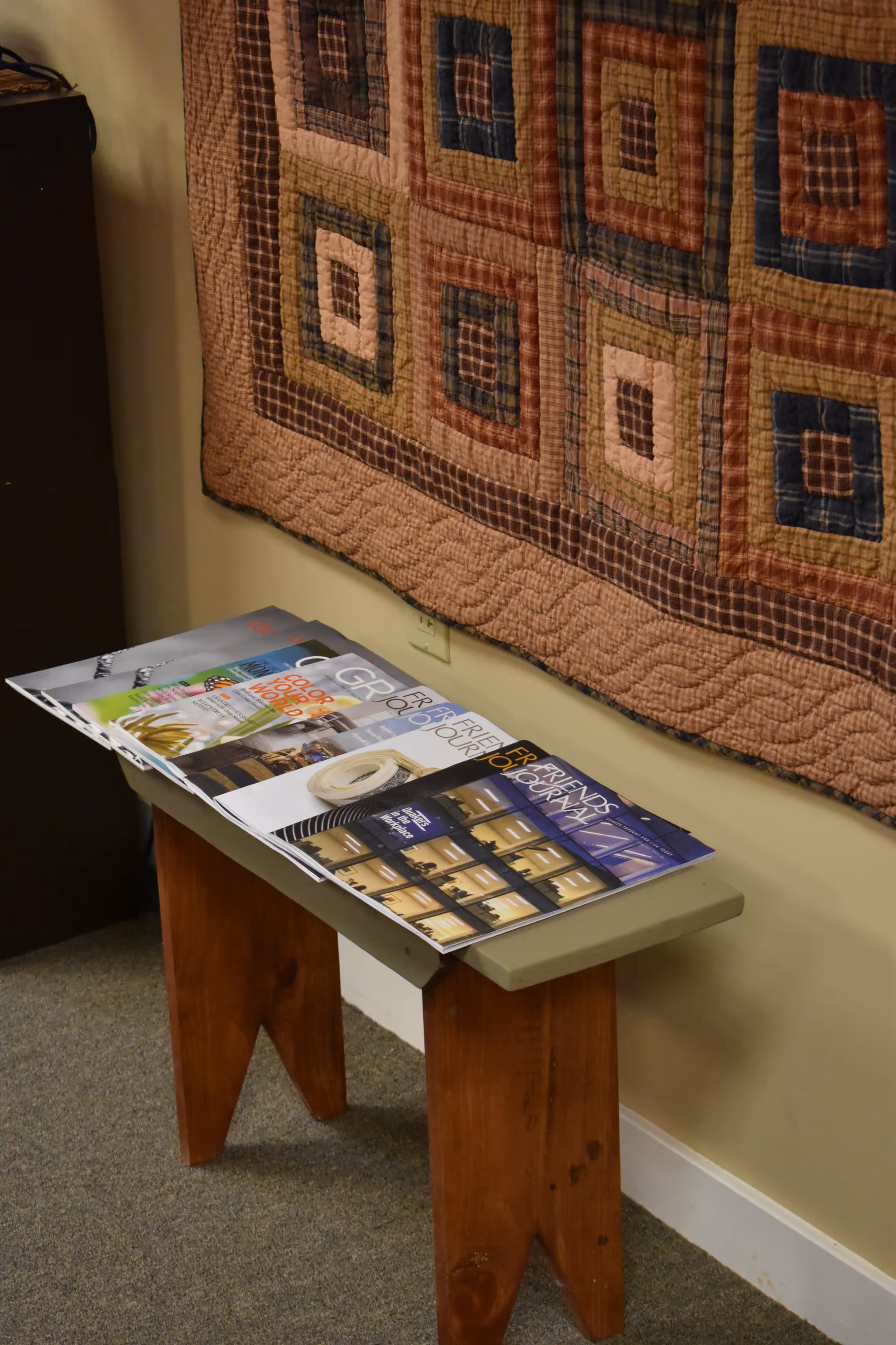BAYADA Hospice interior hallway shows a patchwork quilt on the wall and magazines on a table.