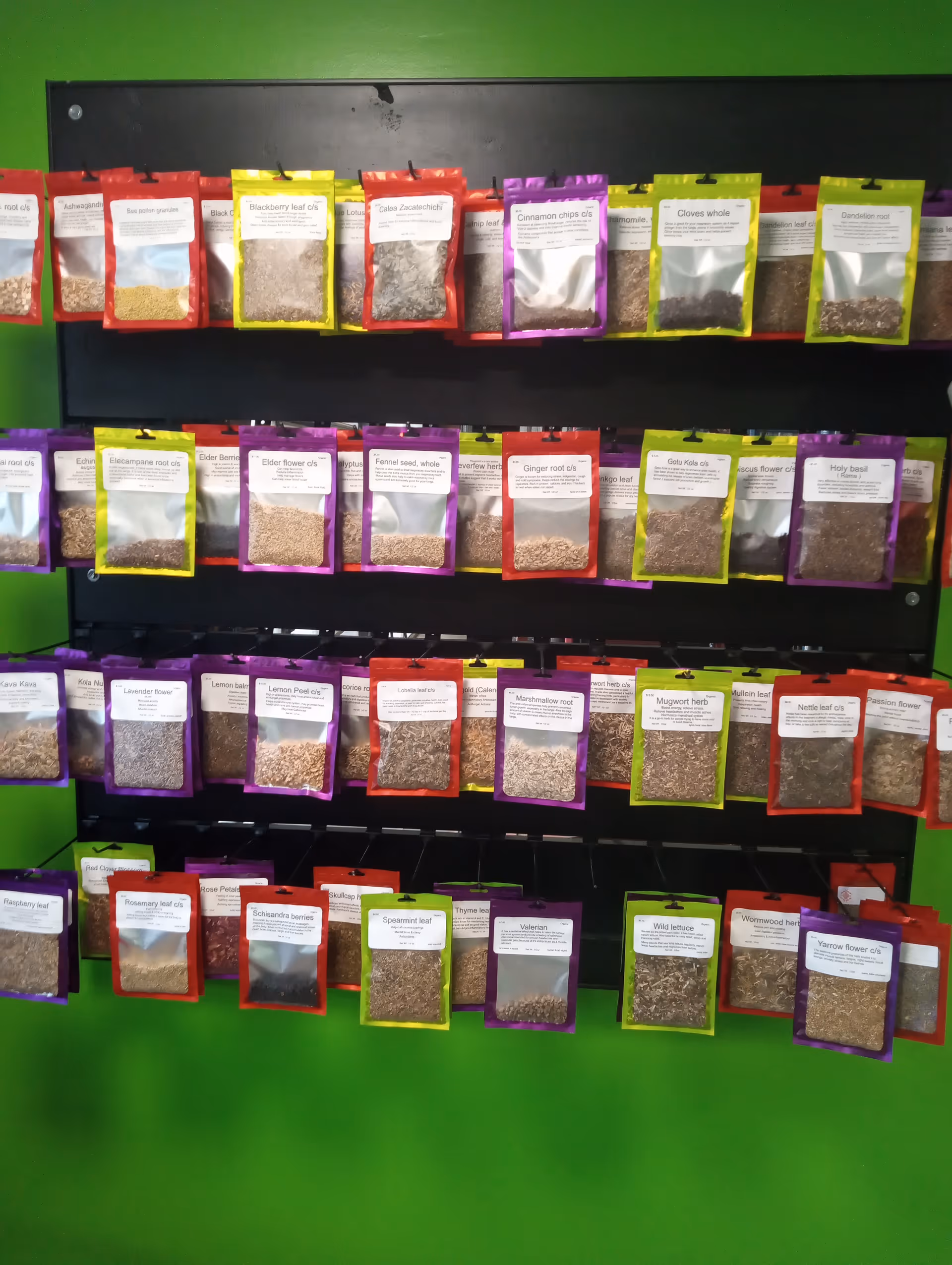 Rows of colorful herb packets on a black rack against a bright green wall.