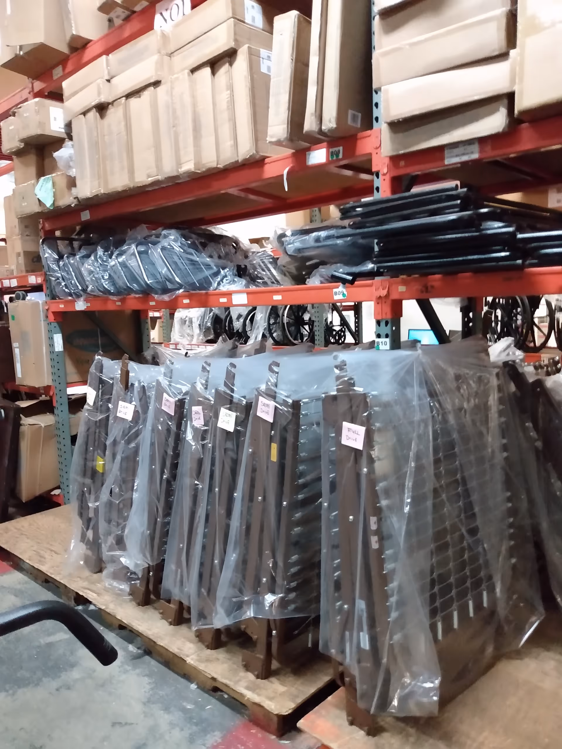 Warehouse storage area with red metal racks, boxed items, and plastic-wrapped equipment.