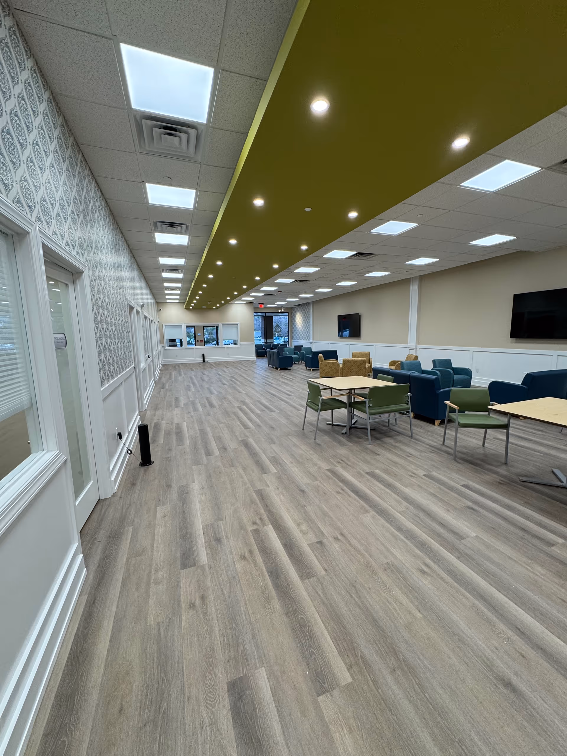 Bright senior living common area with modern seating, tables, and a wall-mounted TV.
