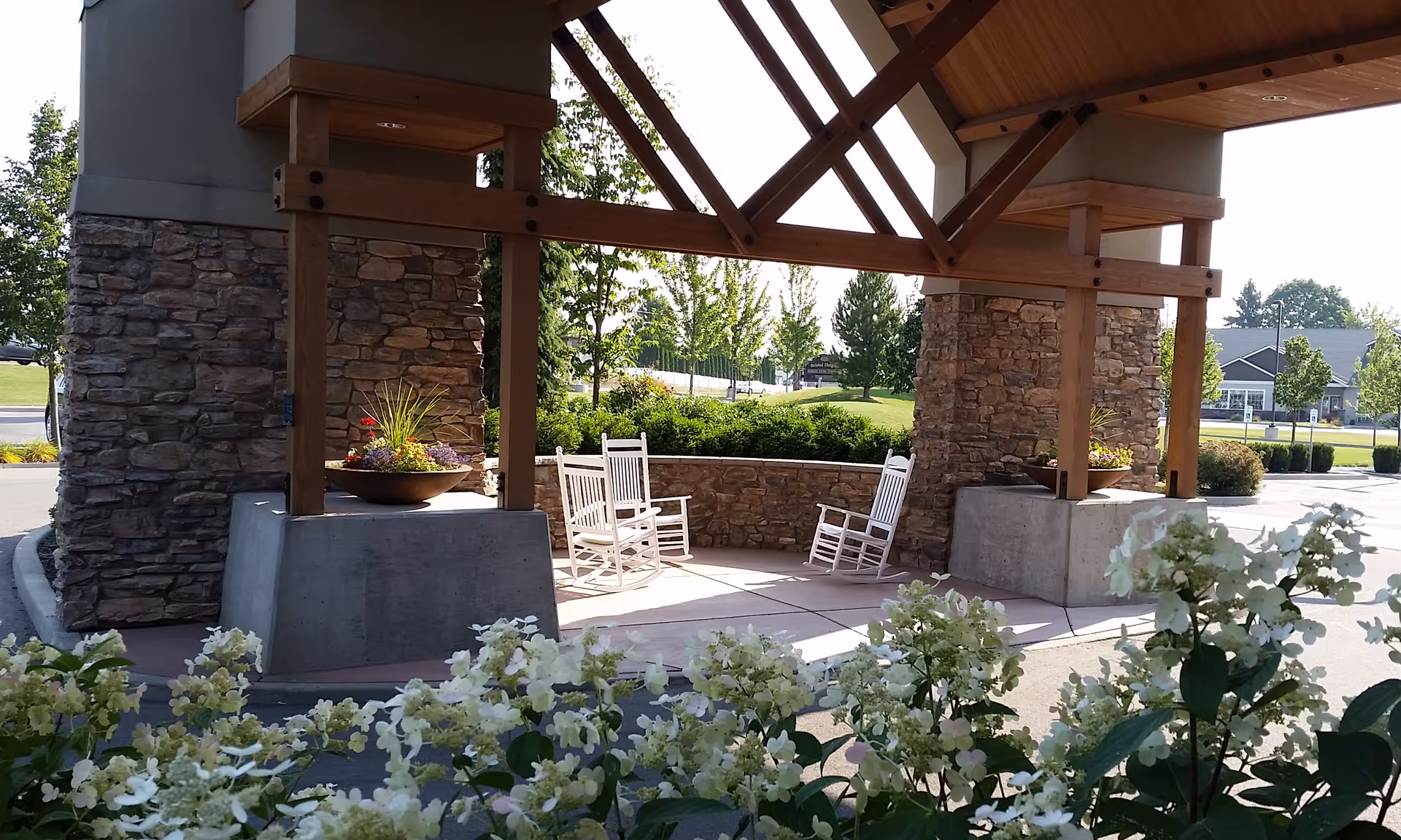 Outdoor patio with white rocking chairs beneath a stone-and-wood pavilion at the entrance.