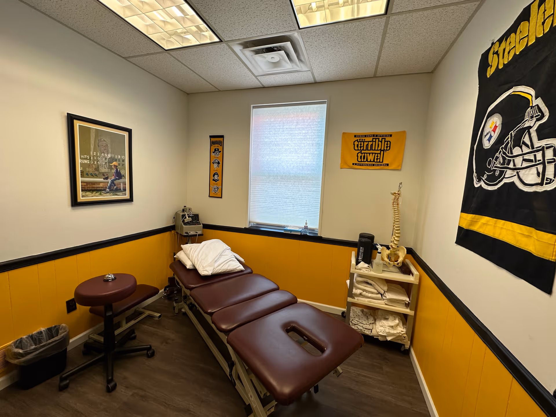 Treatment table in a small clinic room with medical equipment and Steelers banner.