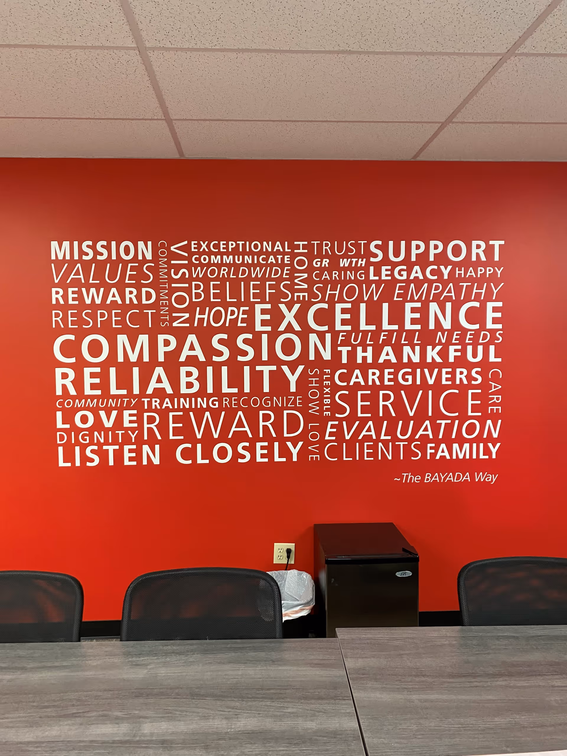 Red wall with white word-cloud art and conference table in a meeting room.