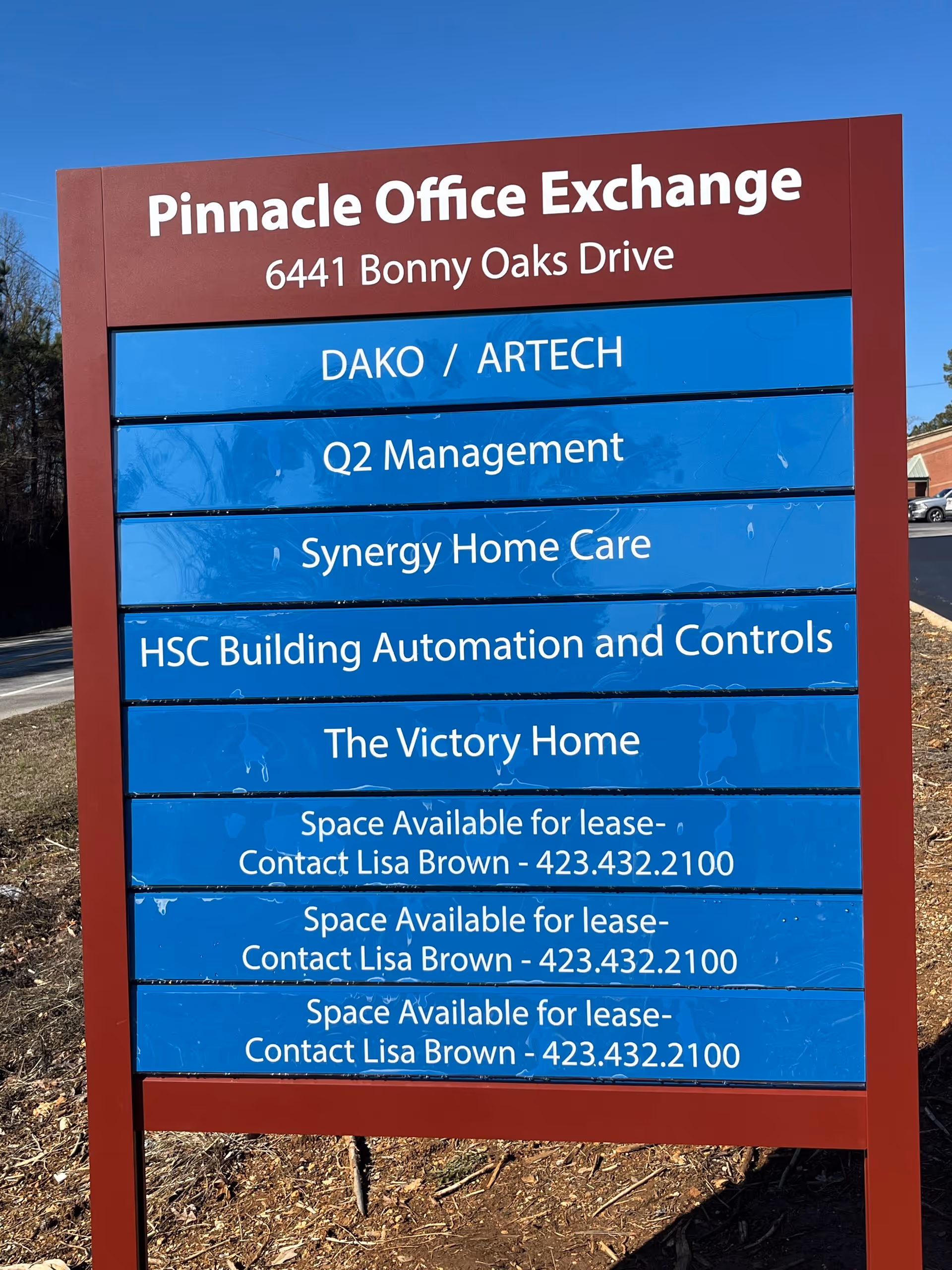 A red-framed sign with blue panels listing tenants outdoors, including Synergy Home Care