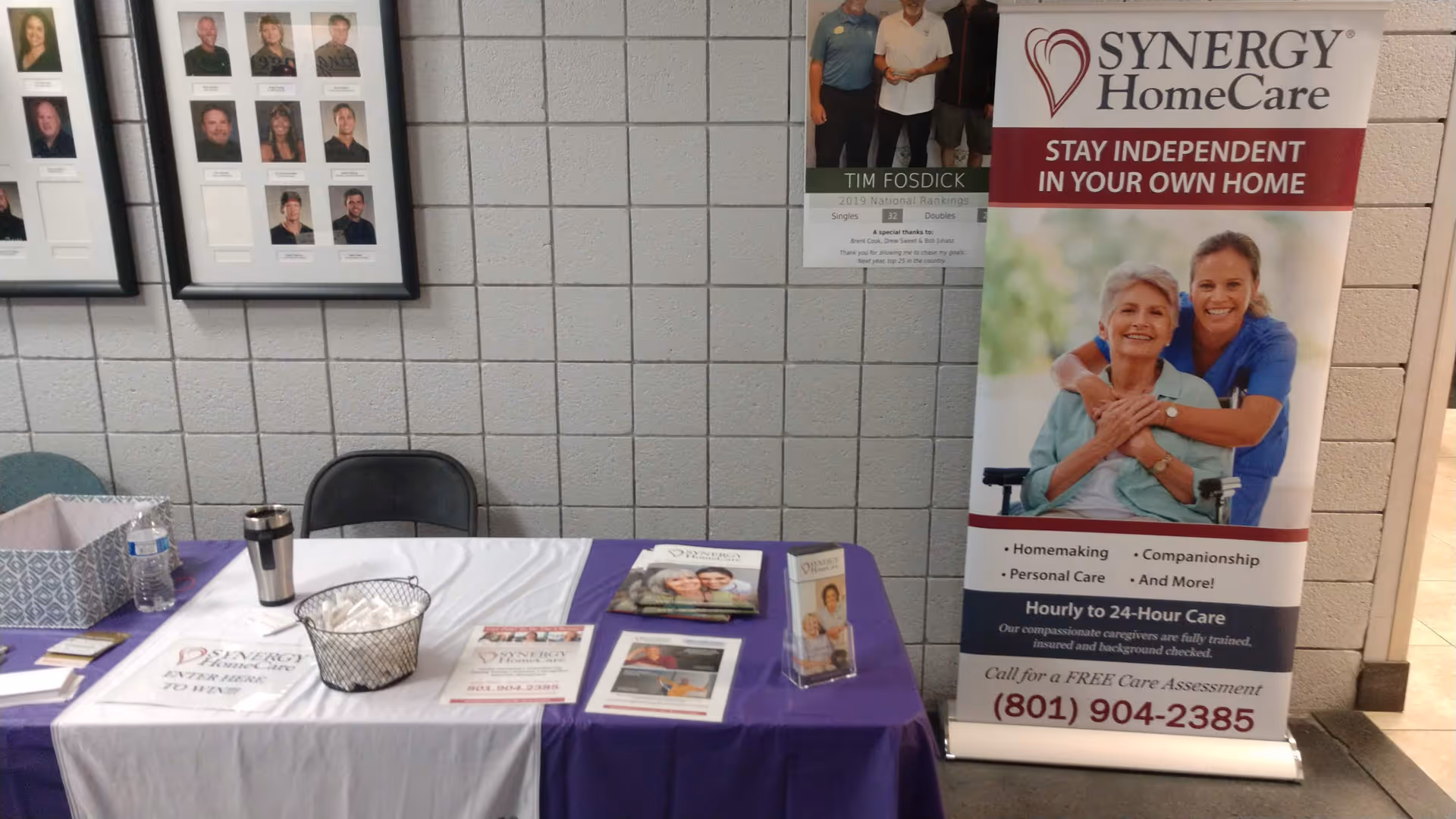 Promotional table and banners for SYNERGY HomeCare in a hallway.