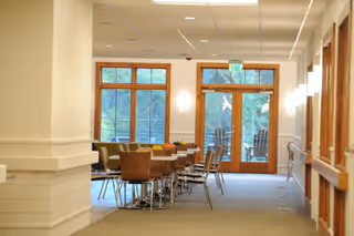 A bright dining area with tables and chairs near large windows and wooden doors.