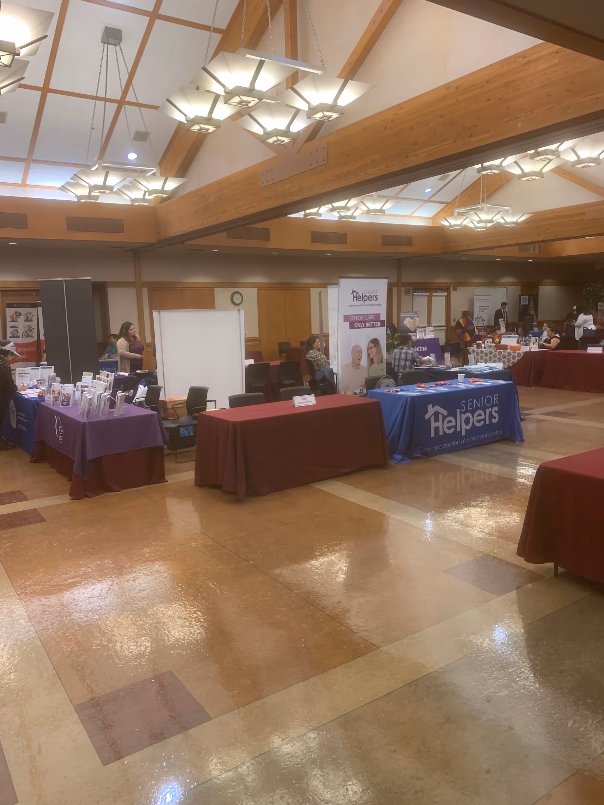 A spacious indoor hall with multiple exhibit tables and banners for Senior Helpers.