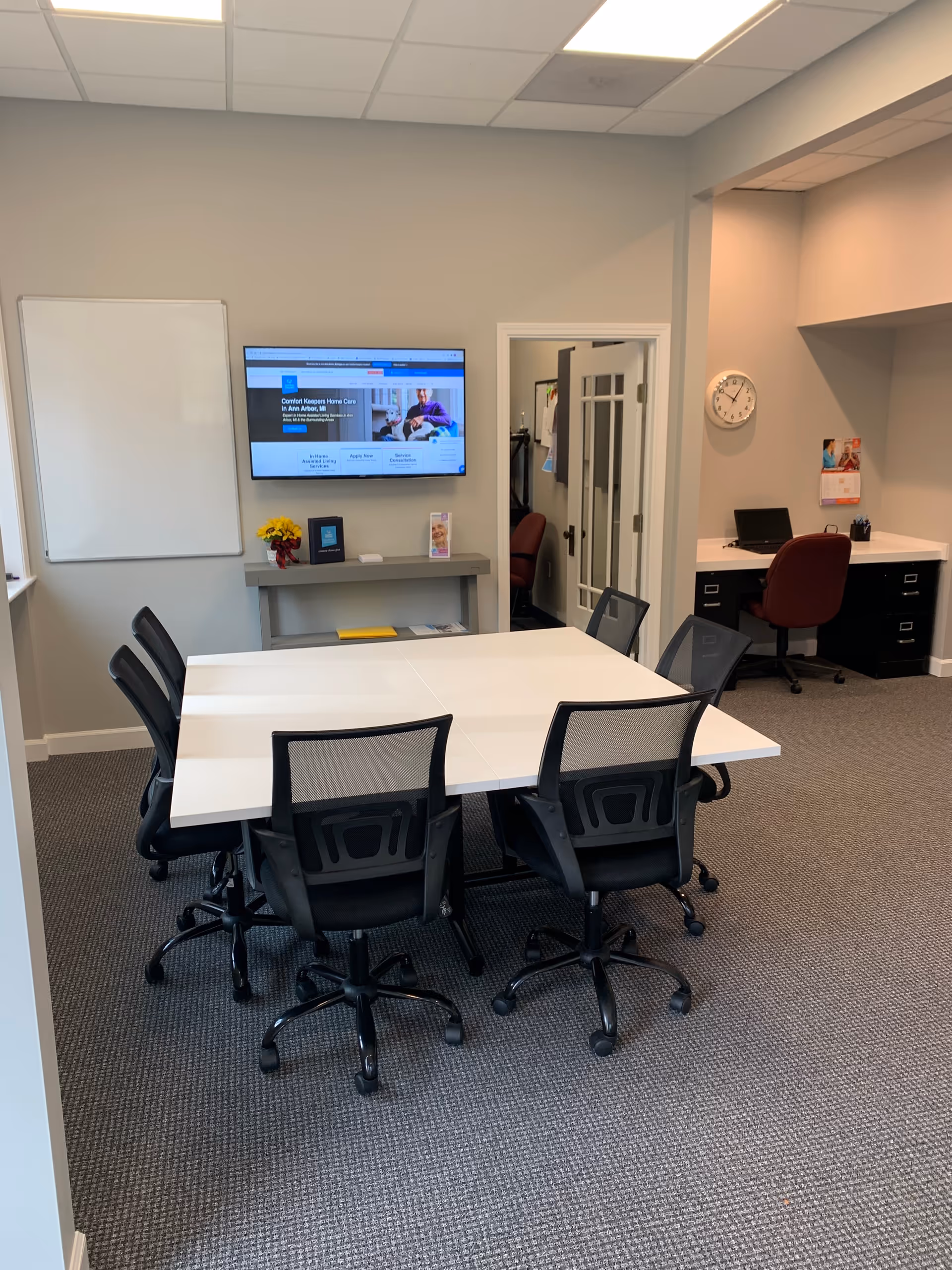 Interior meeting room with white table, black chairs, and wall-mounted TV.