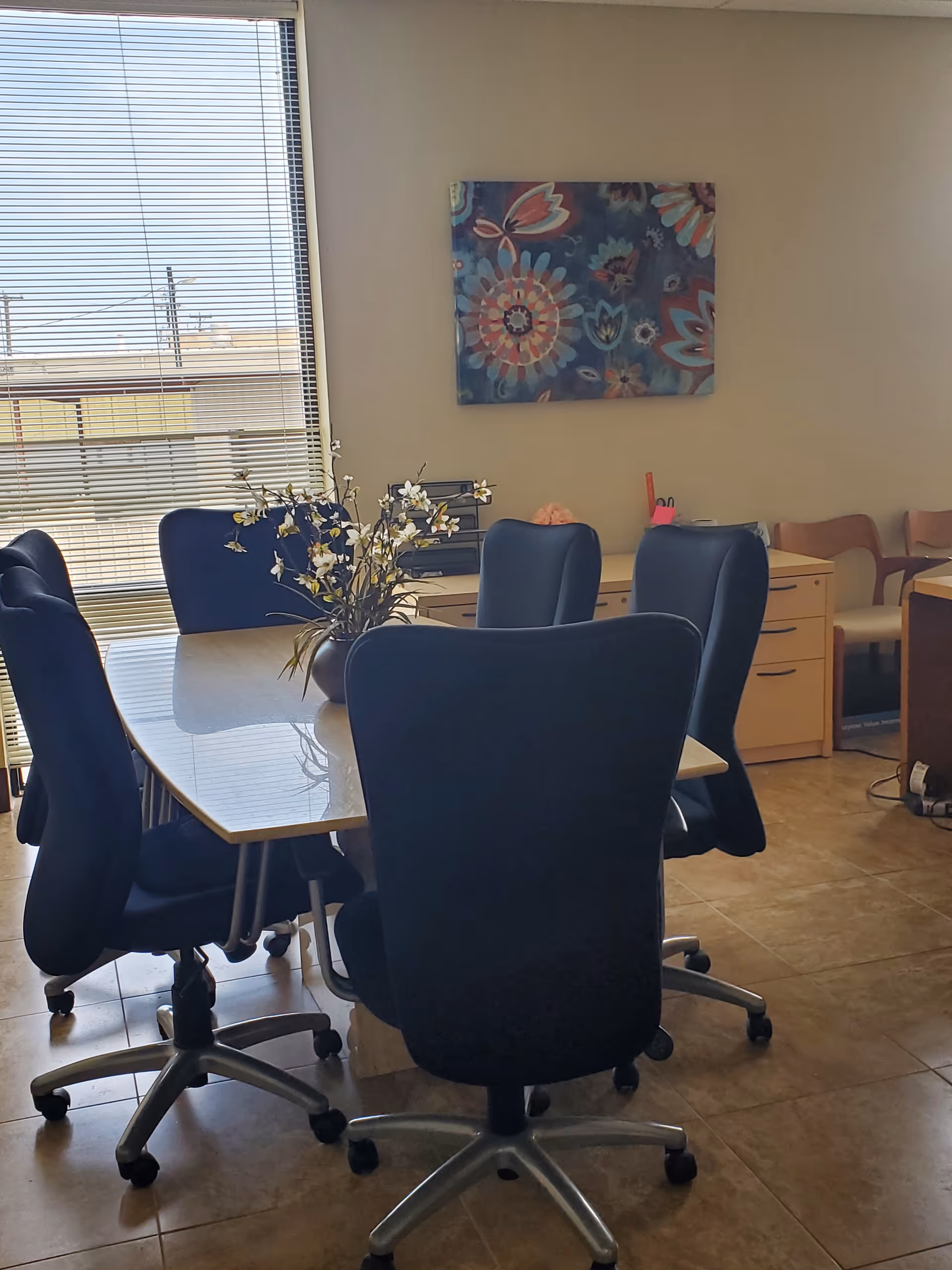 A conference-style meeting room with a glass table, blue chairs, and colorful wall art.