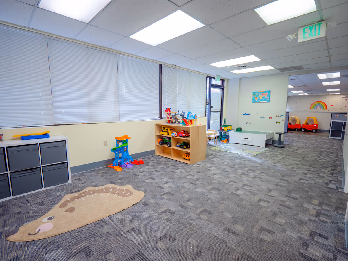 Brightly lit indoor play area with toy shelves, vehicles, and a rainbow mural.