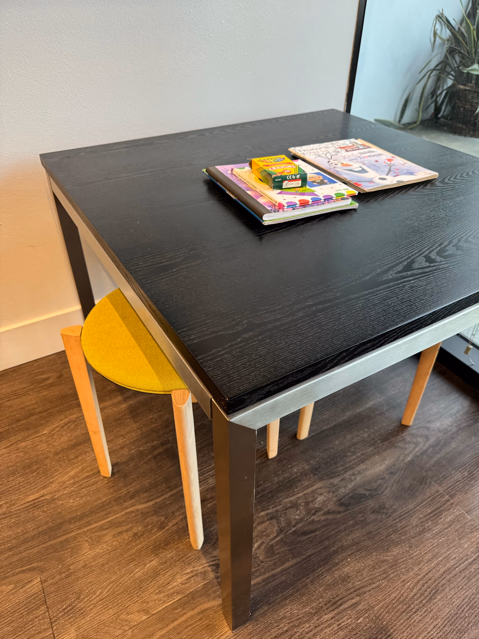 Black dining table with magazines and a yellow chair in a bright room