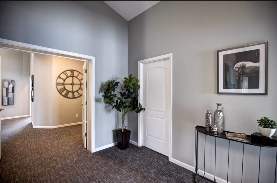Interior hallway of a senior facility with gray walls, doorway, plant, and console table.