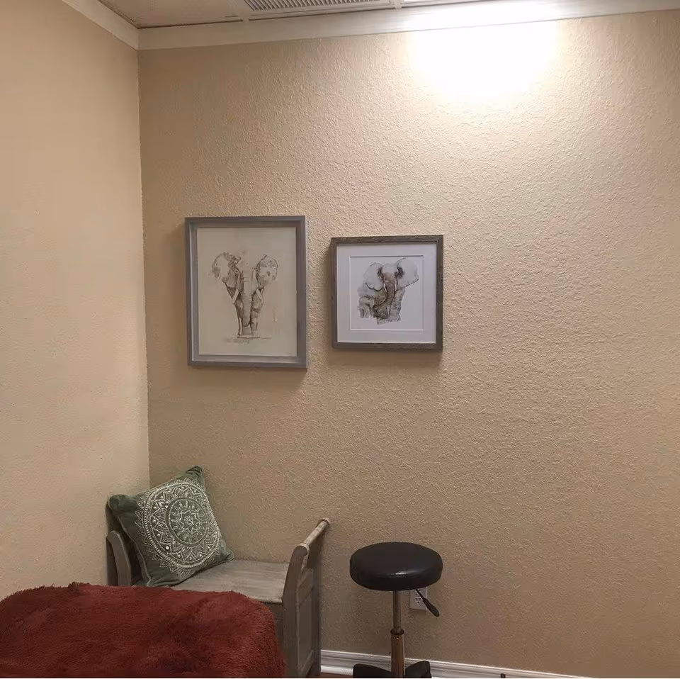 Corner bedroom with bed, green pillow, red blanket, wall art, and a stool.