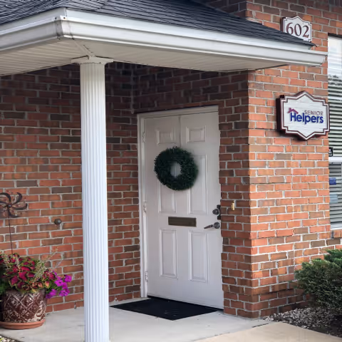 Brick building entrance with a white door, wreath, and Senior Helpers sign.