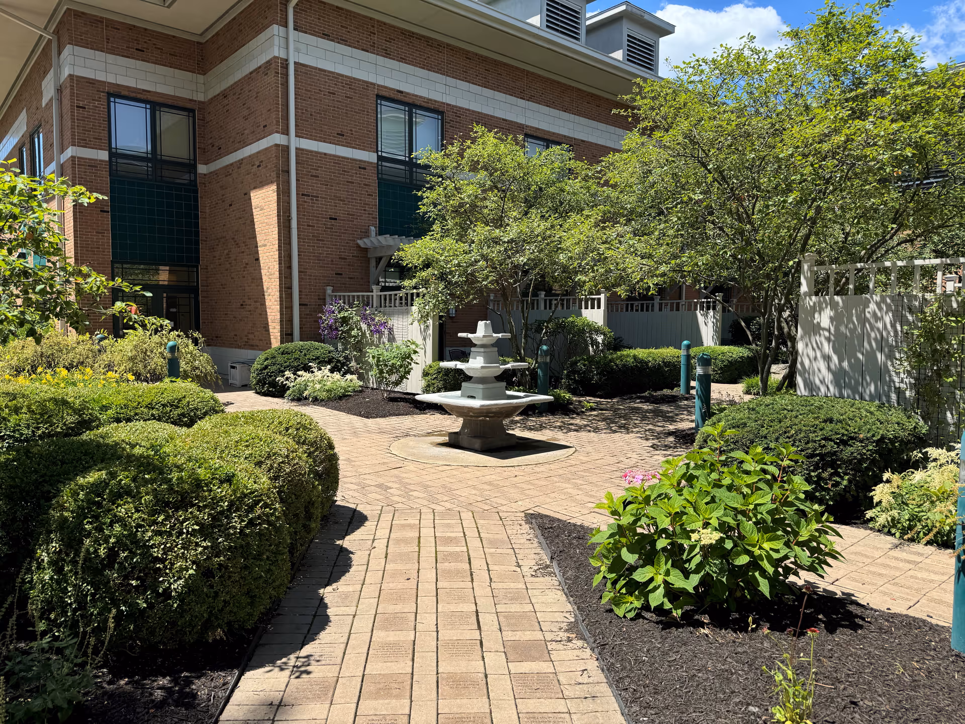 Brick building with a paved courtyard, central fountain, and lush landscaping.
