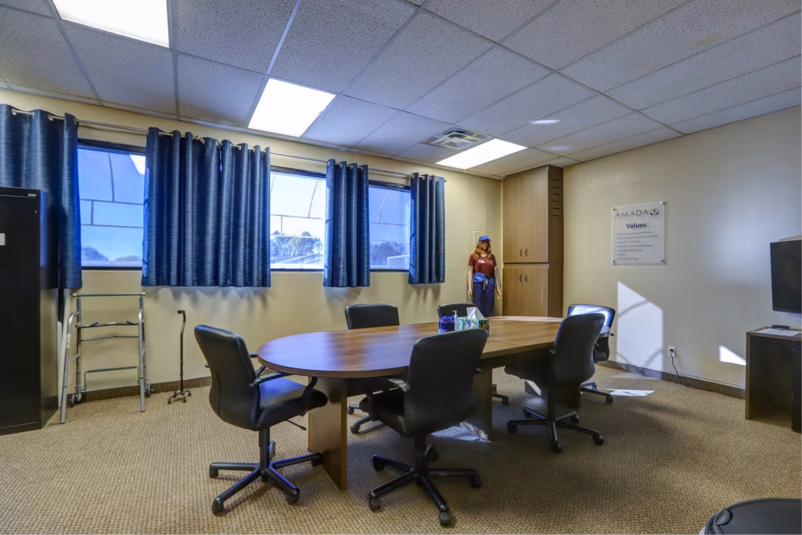Round wooden table with black chairs in a bright meeting room with blue curtains.
