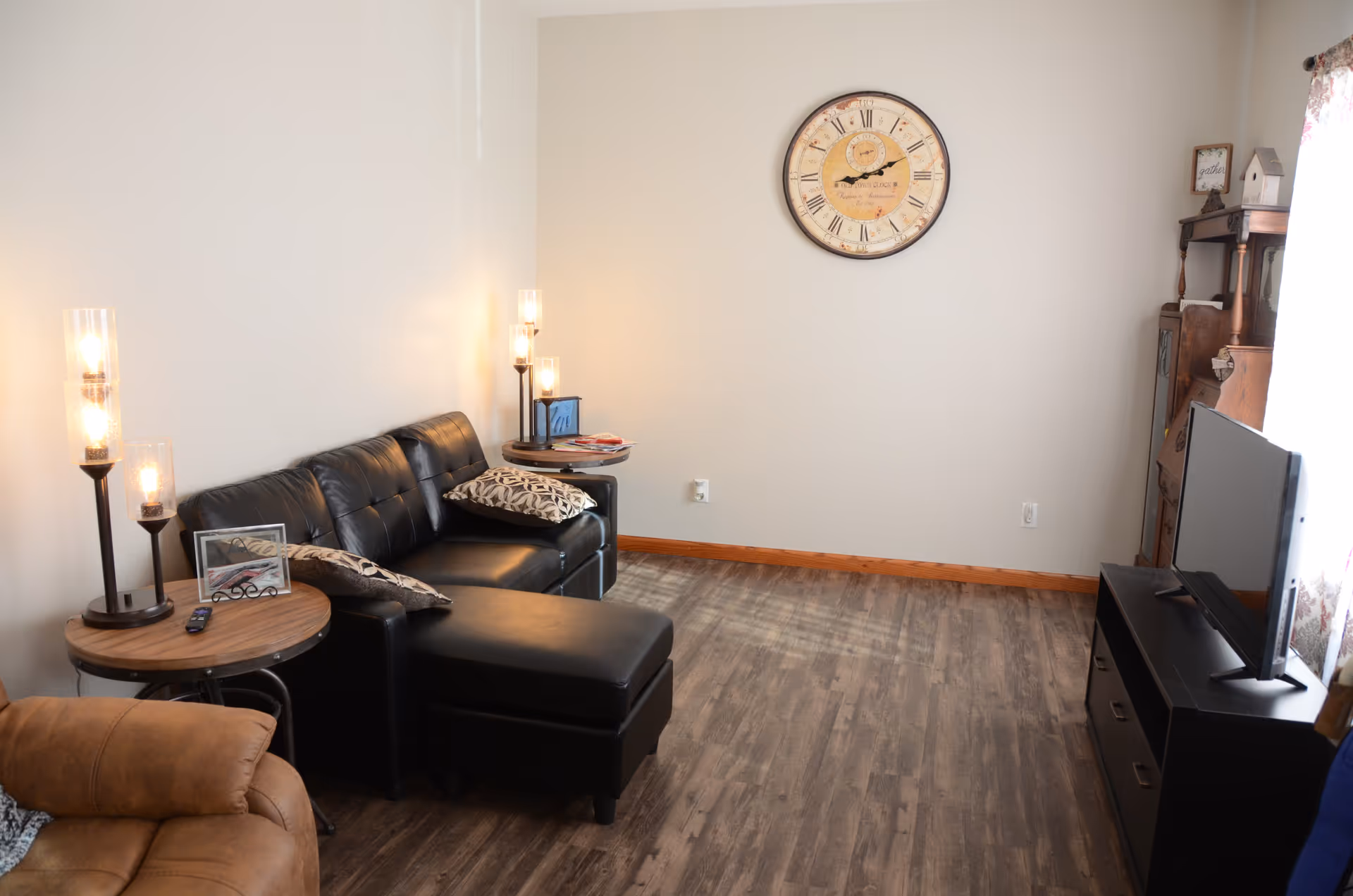 Cozy living room with leather sofa, lamps, clock, and TV stand.