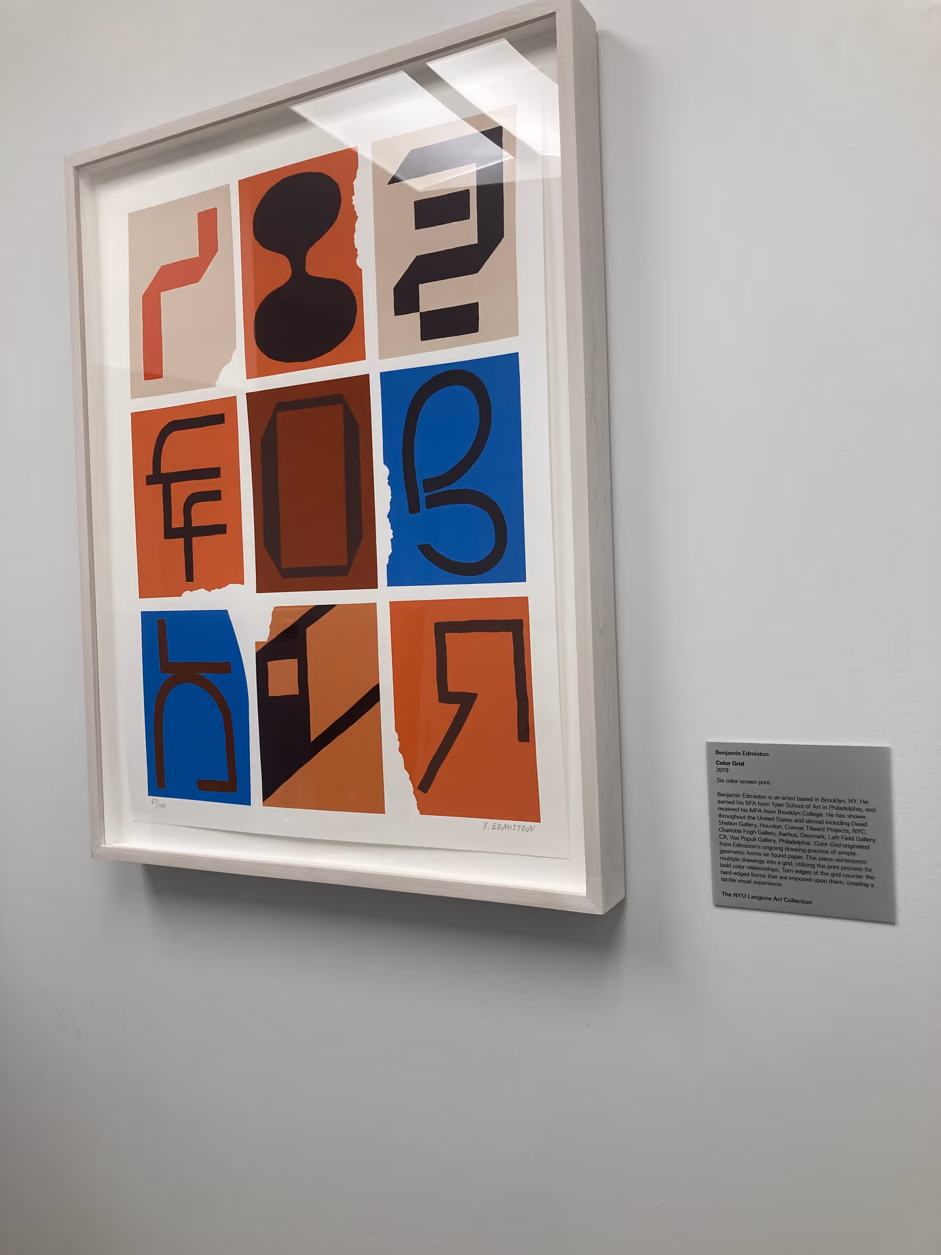Framed abstract artwork hangs on a light wall beside a small plaque.