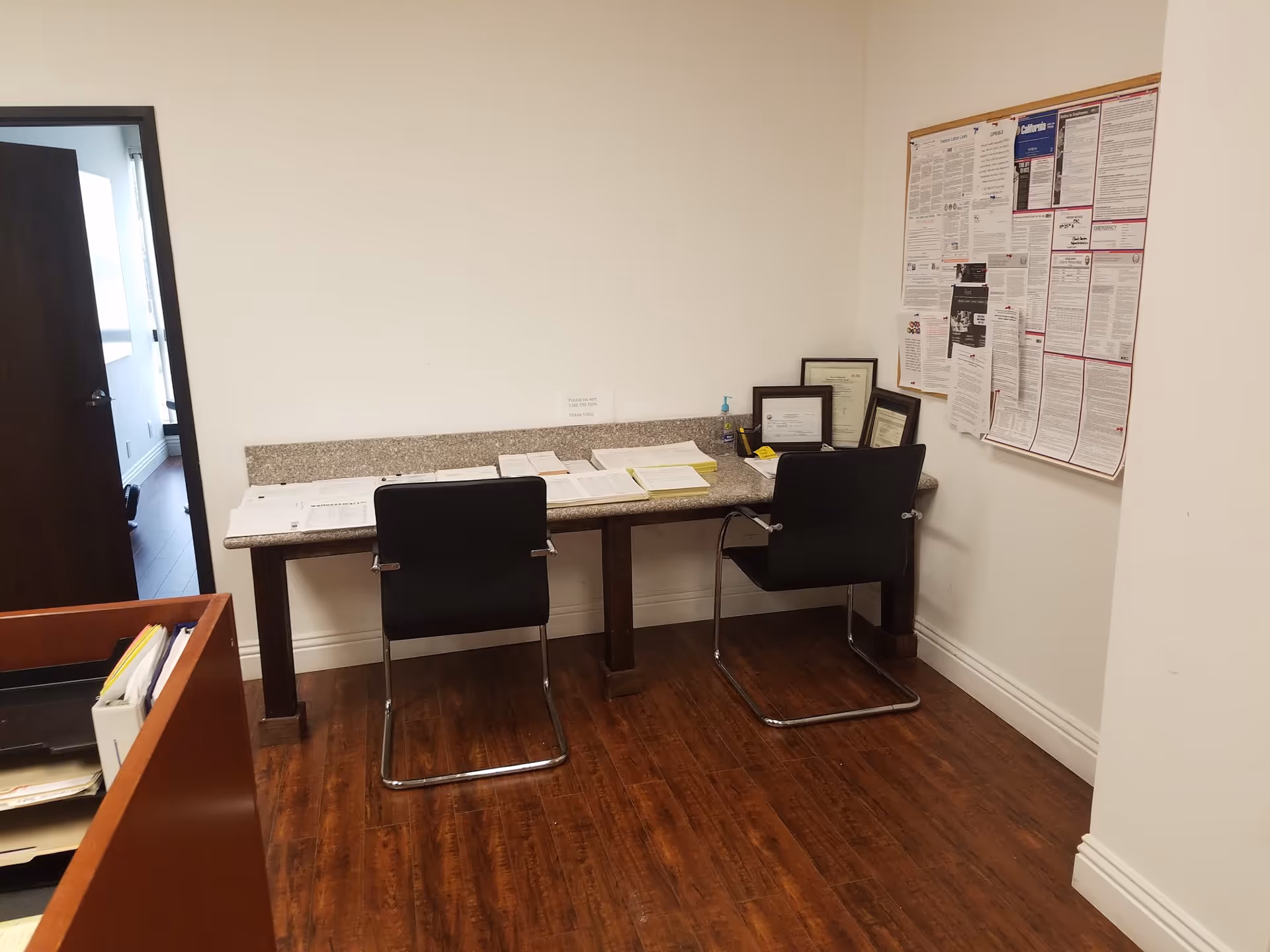 Small office workspace with a long desk, two chairs, and bulletin board.