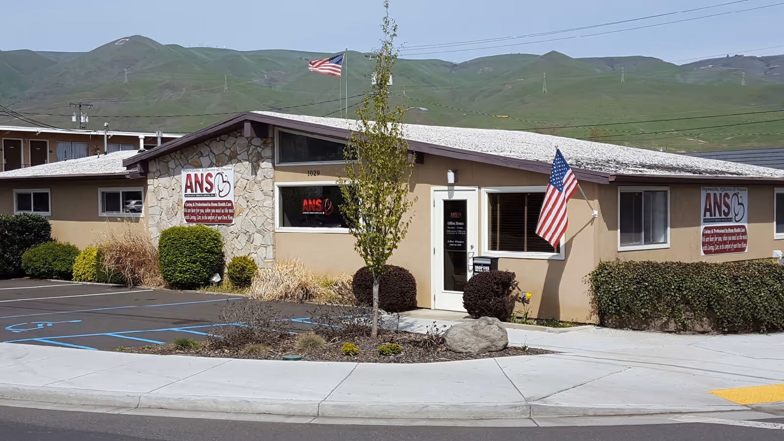 Exterior view of Alternative Nursing Services, Inc. building with stone accents and flags.