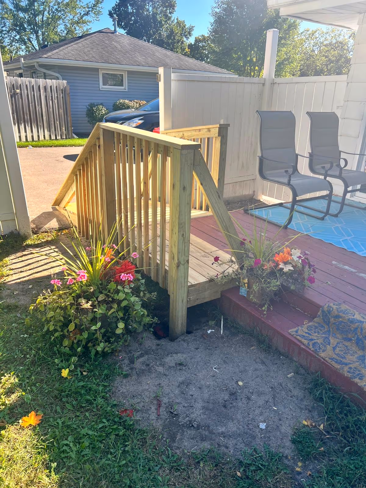 Outdoor wooden deck with stairs, two chairs, potted flowers, and a white fence.