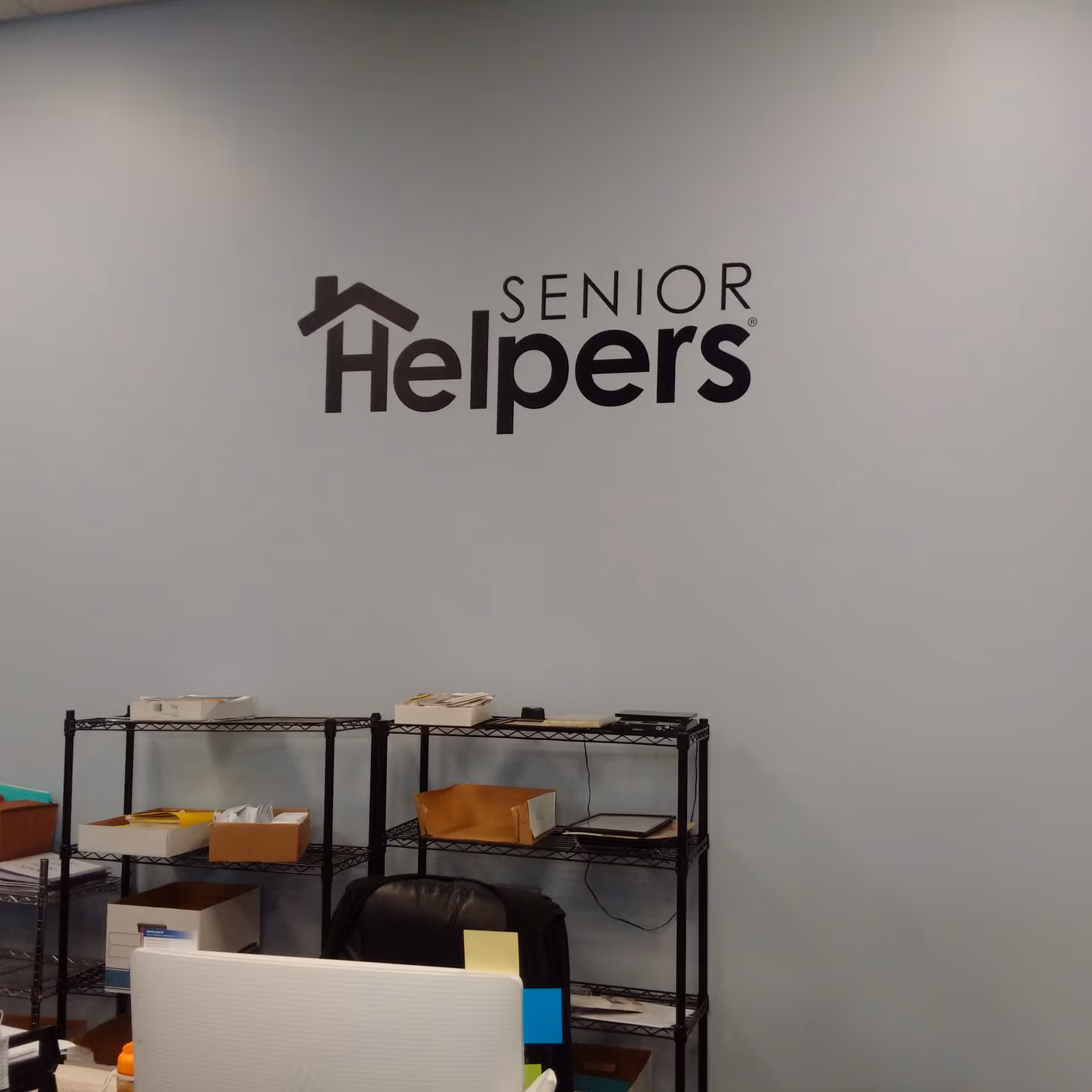 Reception area with Senior Helpers logo on a light blue wall and shelving units.