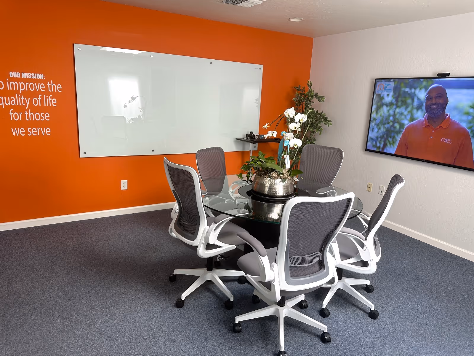 A glass conference table with six chairs in an orange-walled meeting room.