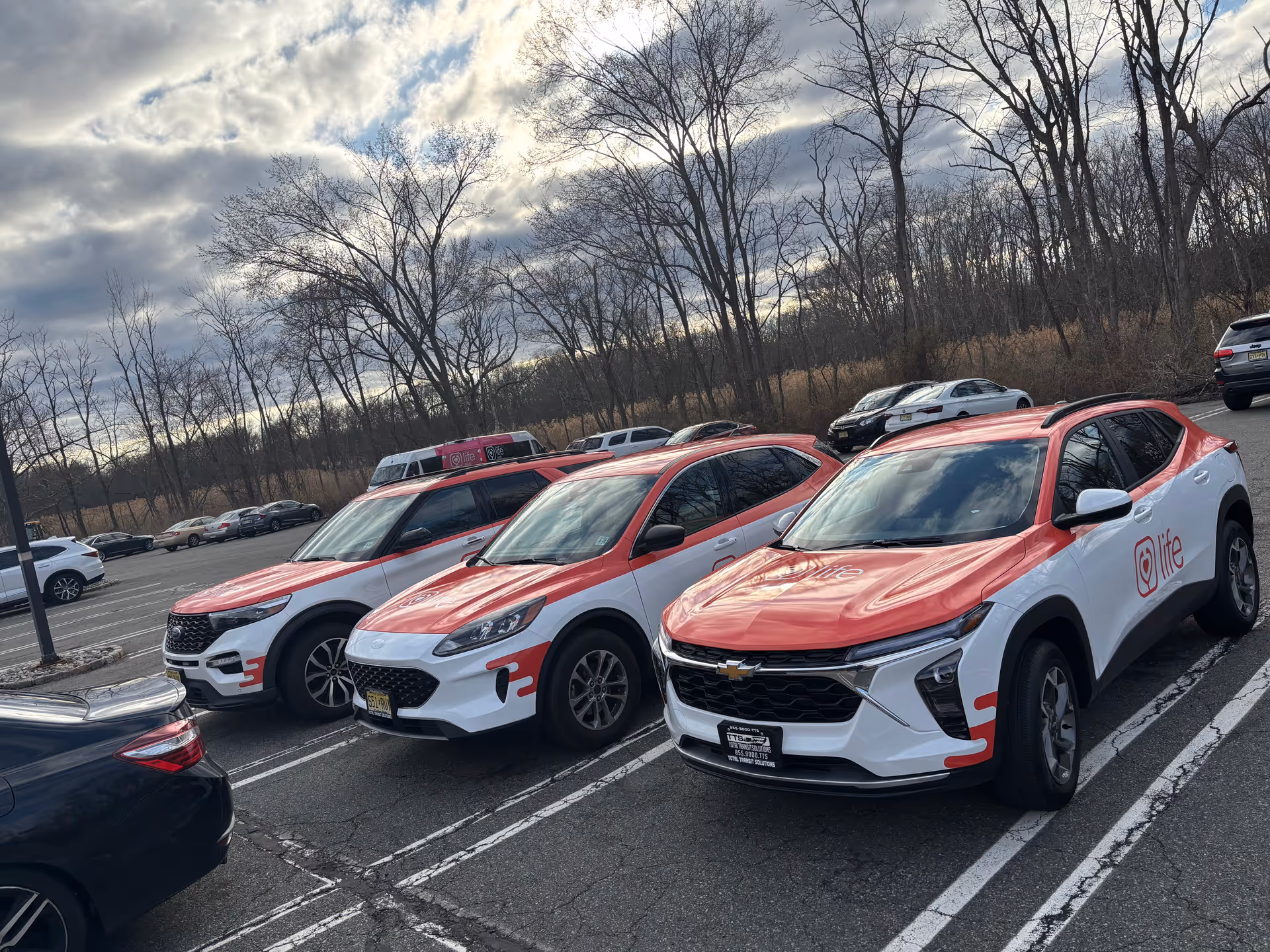 Several red and white branded Life Medical vehicles parked in a lot with bare trees.