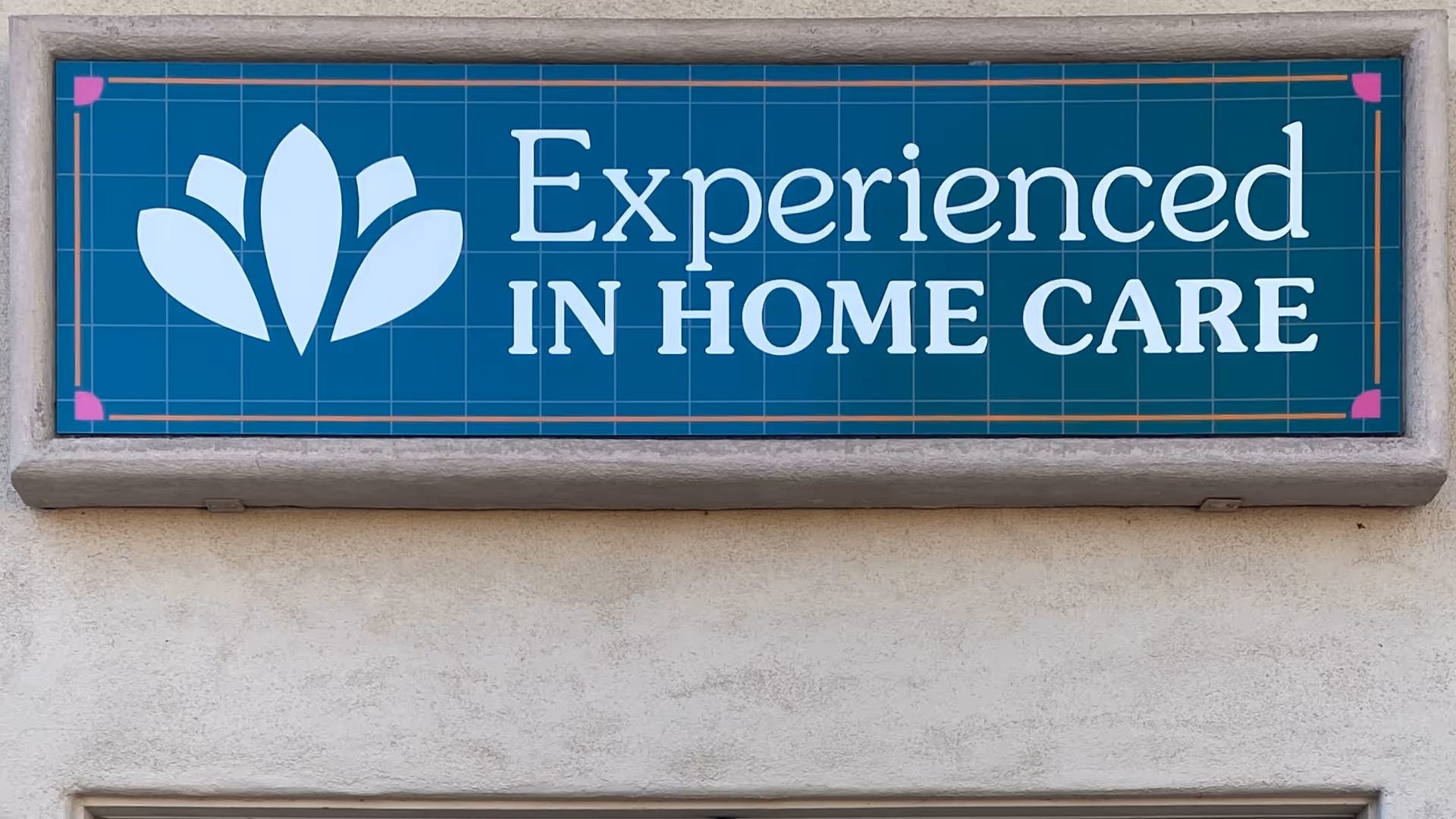 Teal sign reading 'Experienced In Home Care' mounted on beige building exterior