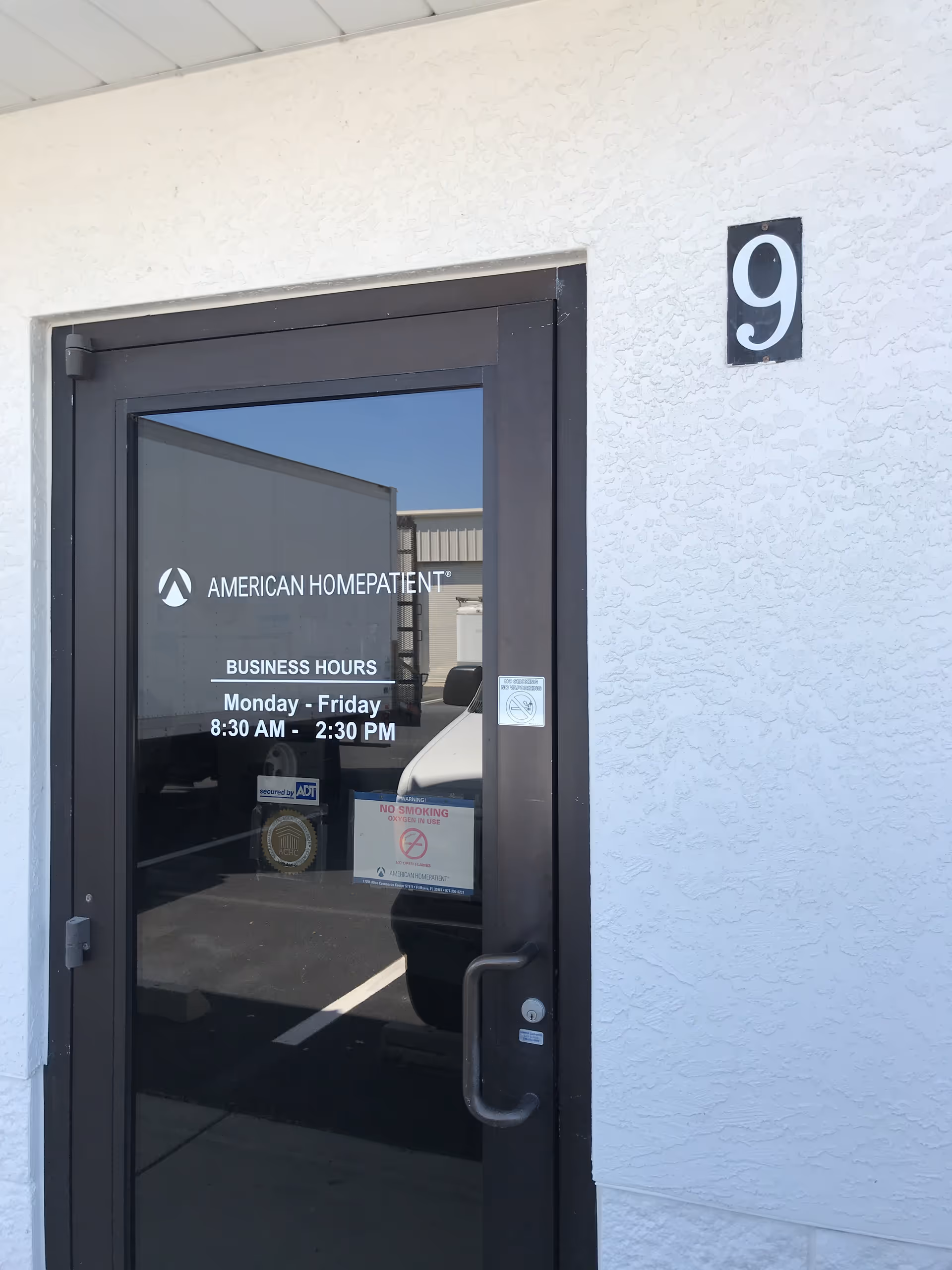 Glass entrance door to American HomePatient with building number 9 and hours posted.