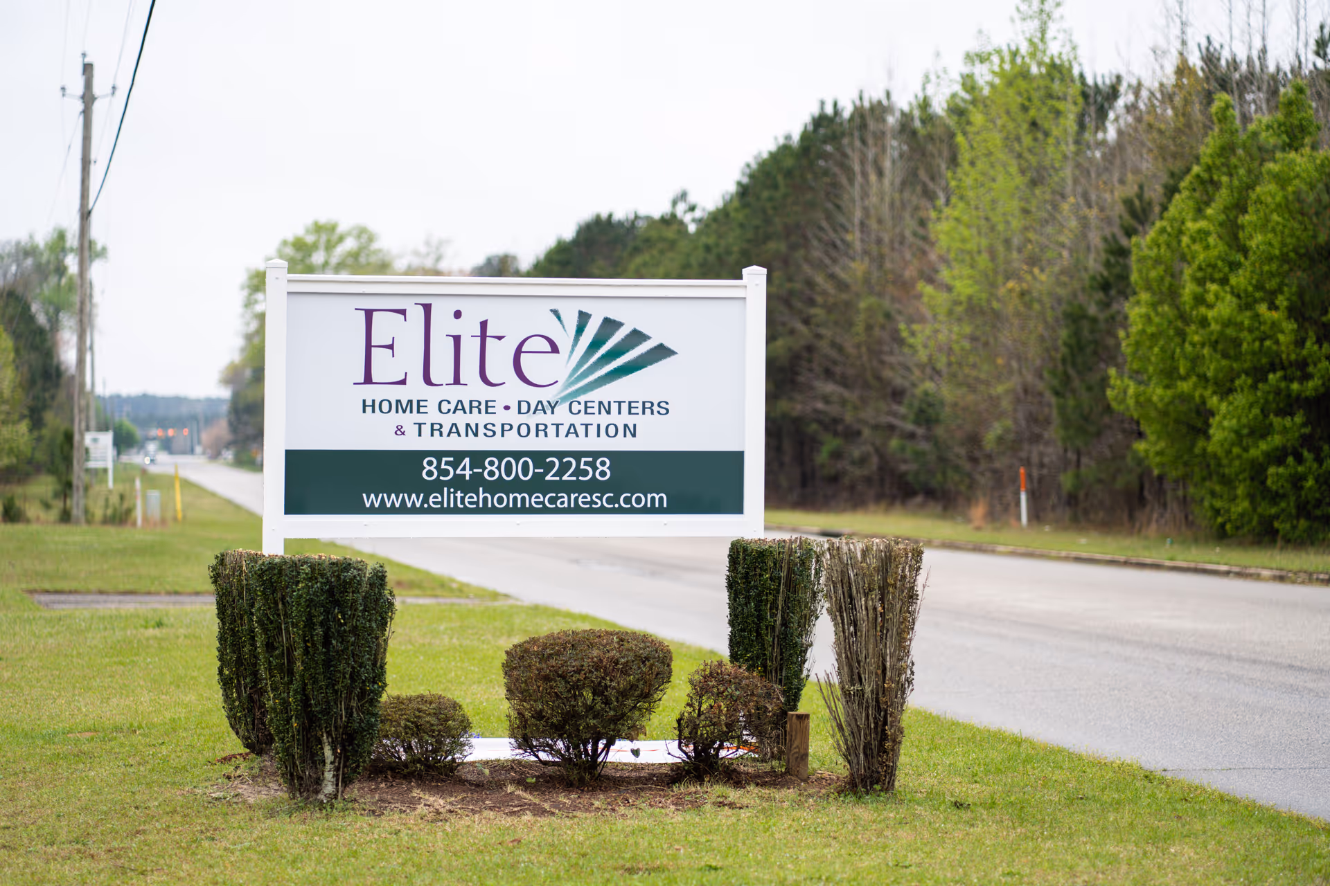 Roadside sign for Elite Home Care Day Centers & Transportation on grassy median