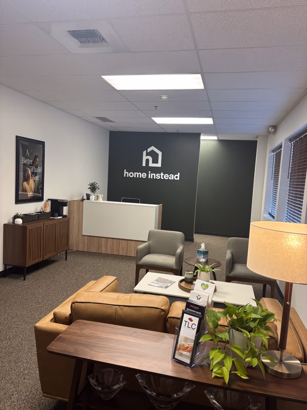 Reception area with a dark wall displaying Home Instead logo, modern seating, and a front desk.