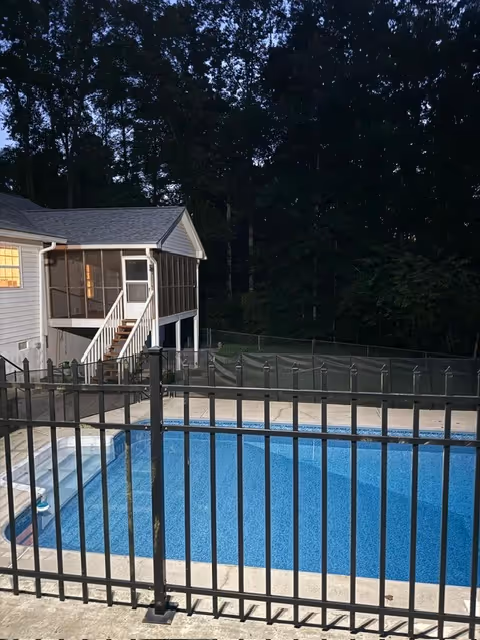 Exterior view of an outdoor pool area with a fenced pool and a screened porch.