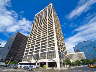 Tall modern skyscraper on a busy city street with surrounding office buildings.