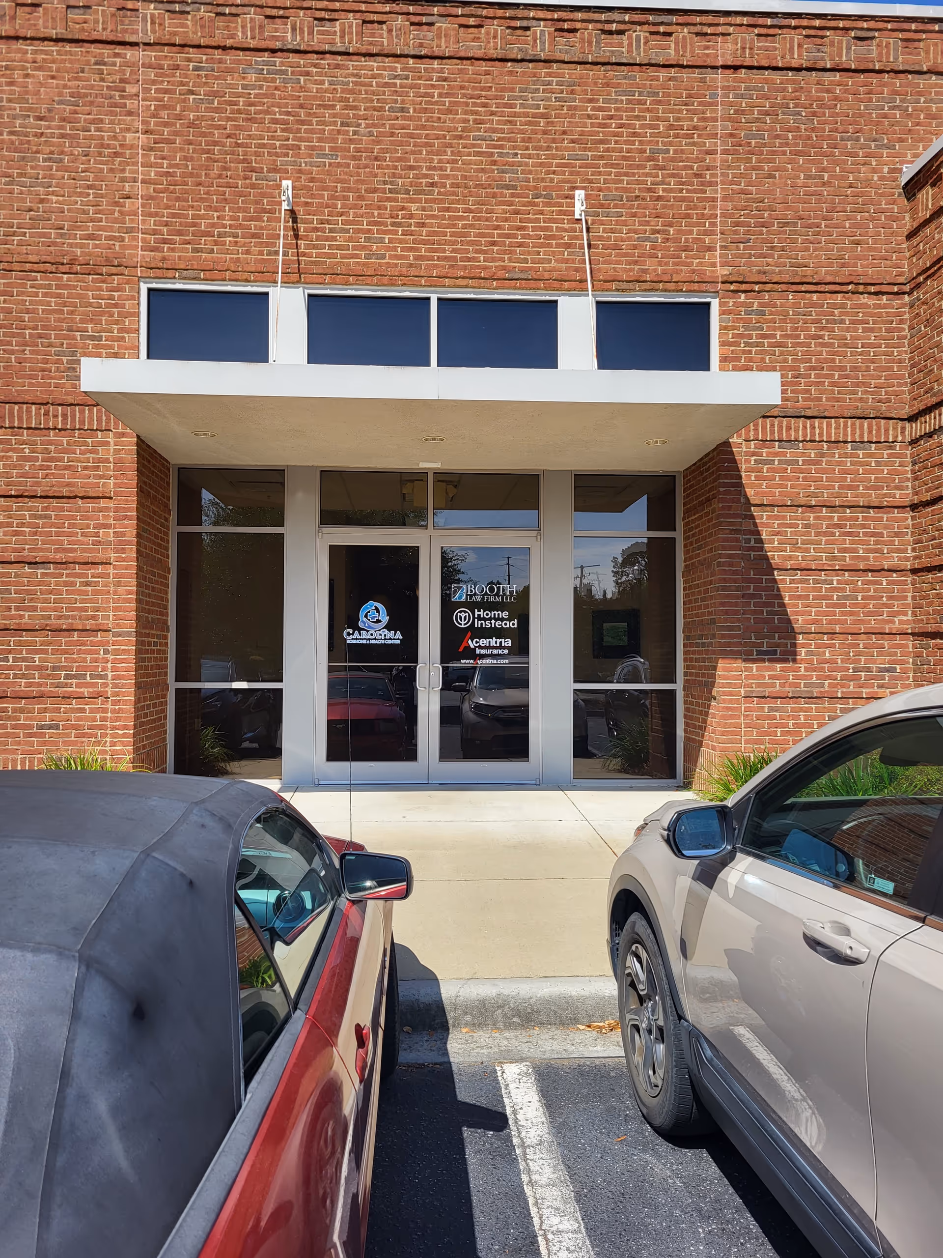 Brick building exterior with glass double doors, white canopy, and parked cars in front.