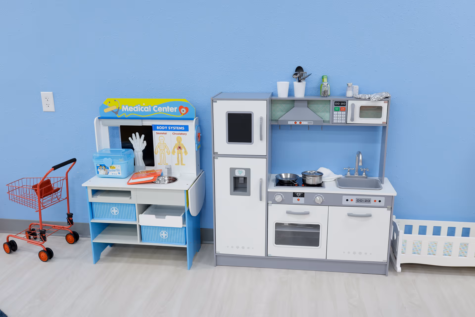 Children's toy kitchen playset against a blue wall with a red shopping cart nearby