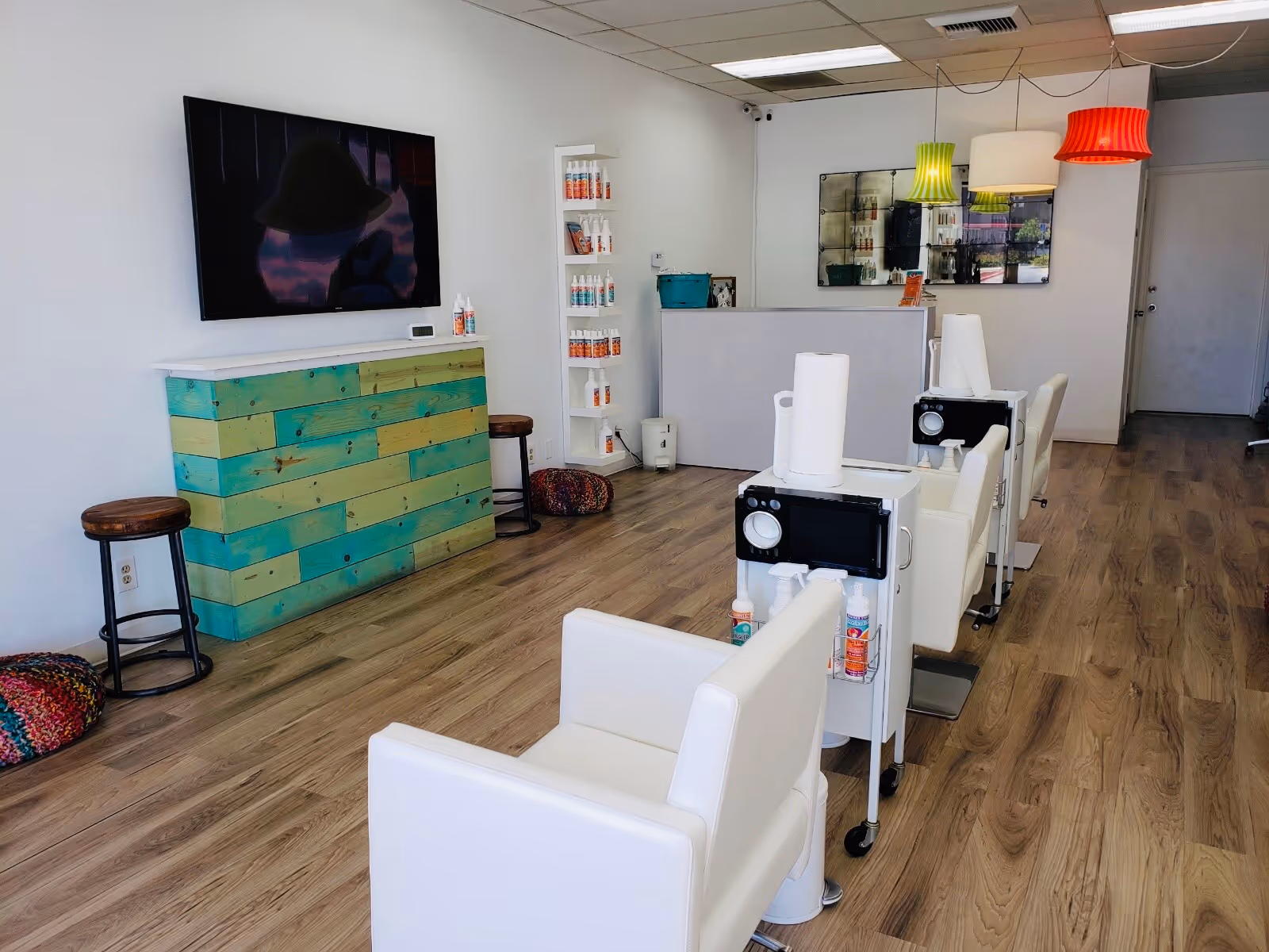 Bright interior salon area with white chairs, carts, product shelves, and a turquoise reception desk.