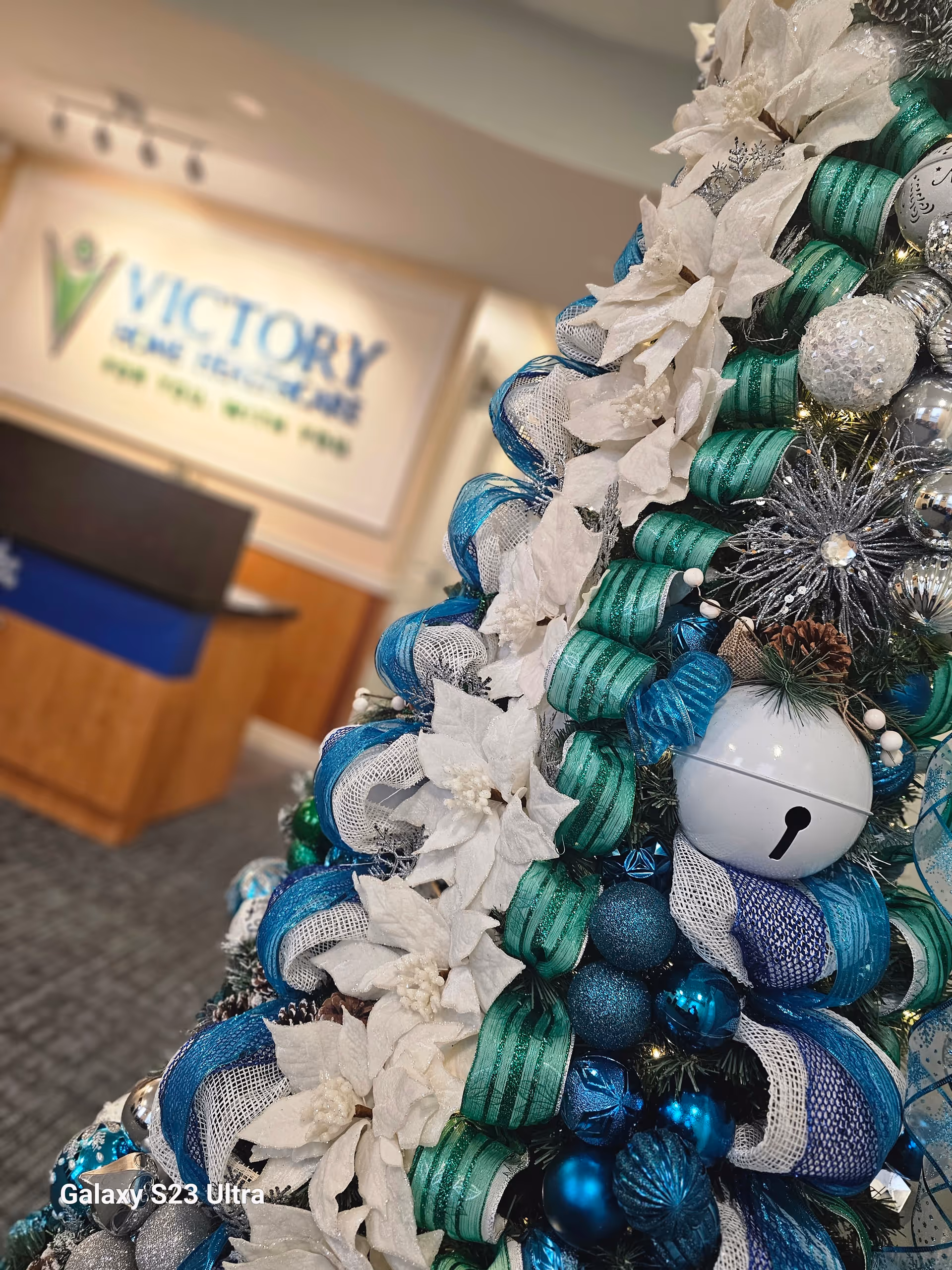 Blue and silver Christmas tree decorates a facility lobby near a Victory Home Healthcare sign.