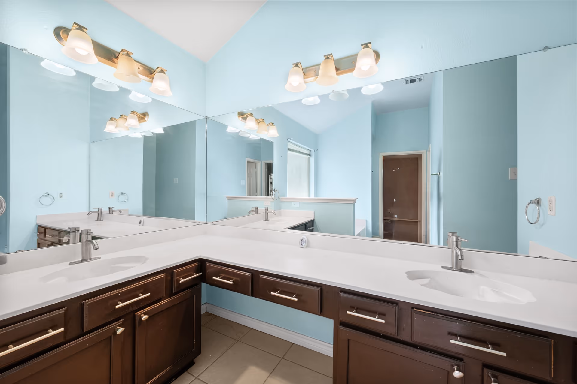 Blue-walled bathroom vanity with two sinks, mirrors, and bright light fixtures.