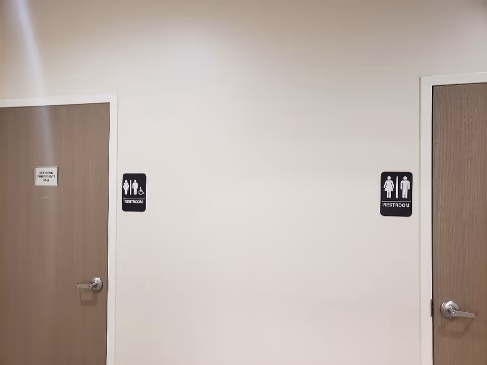 Interior hallway with two doors and restroom signs along a beige wall.