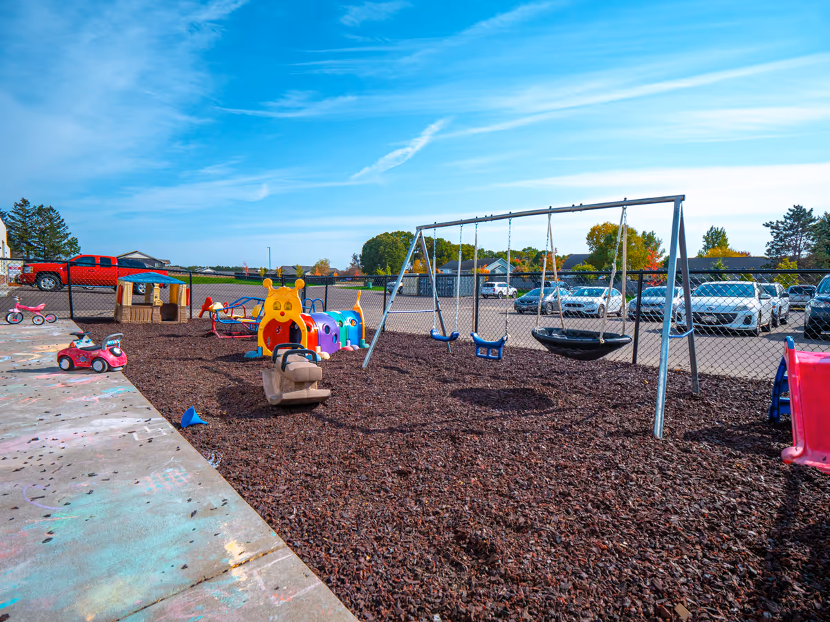 Outdoor playground with swings, colorful structures, and a chain-link fence surrounding the area.