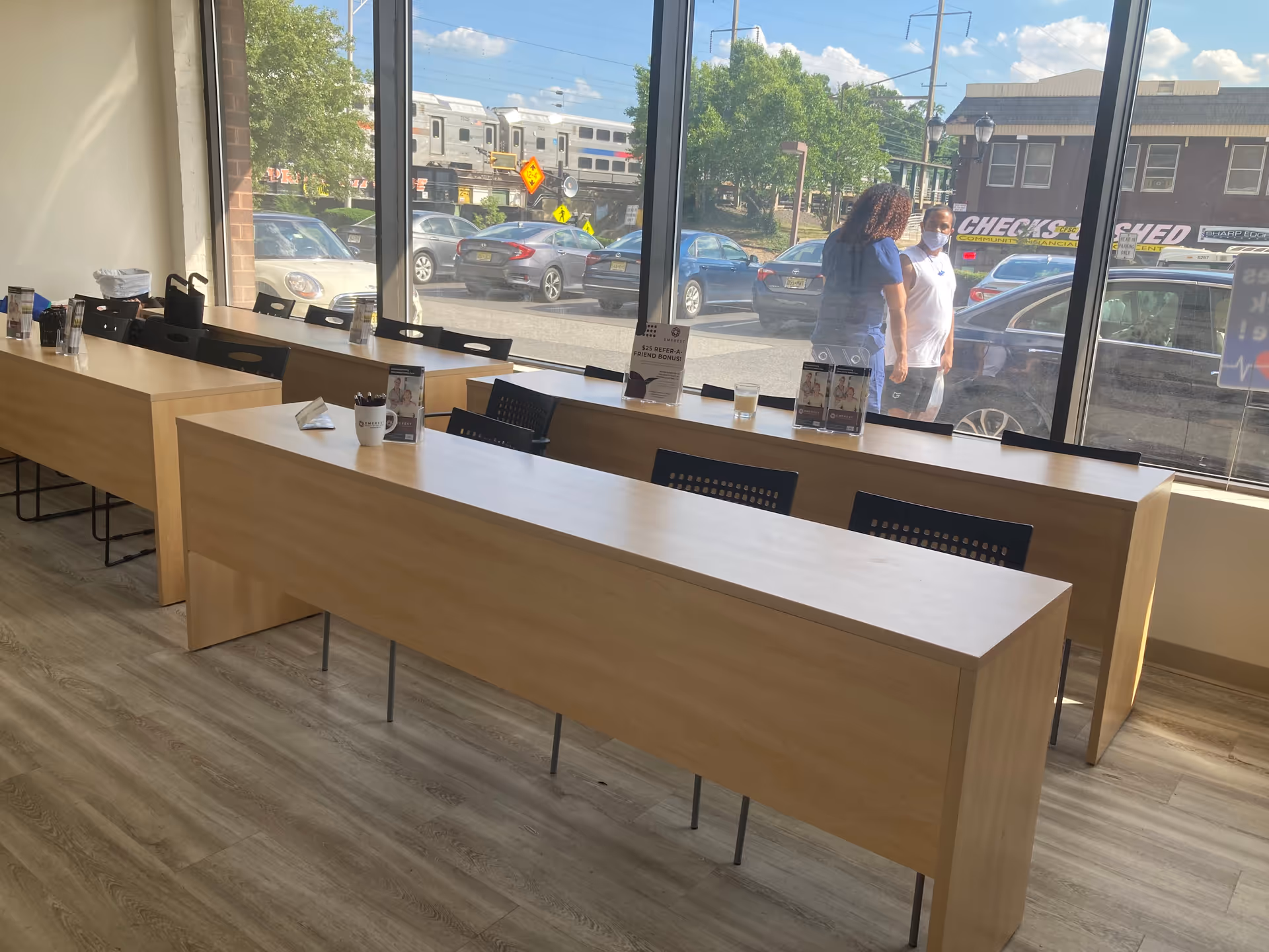 Bright interior with long wooden tables and chairs by large windows in a communal dining area.